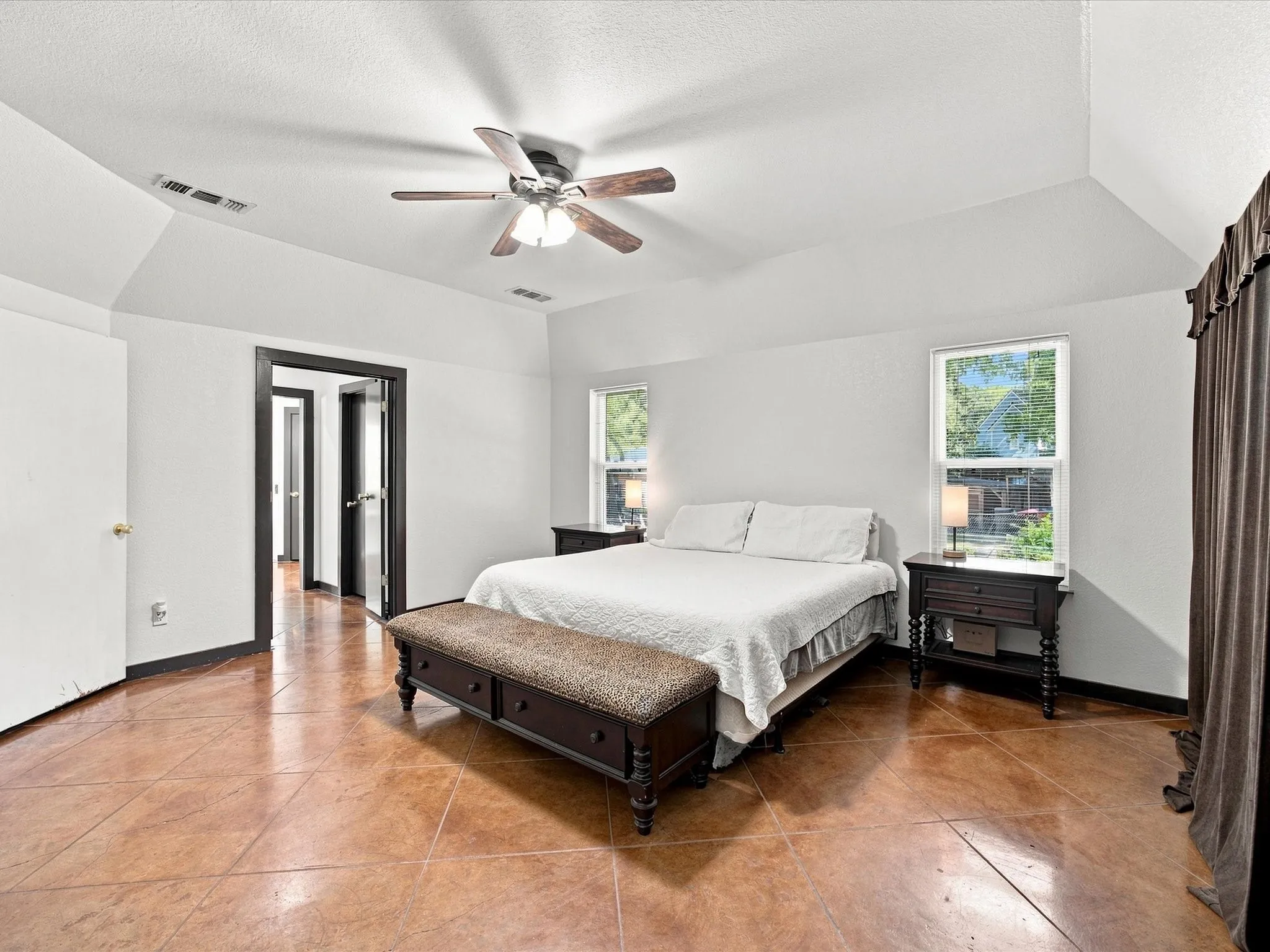 Vaulted ceiling with ceiling fan, two windows, two paneled doors with dark trim, and tiled flooring