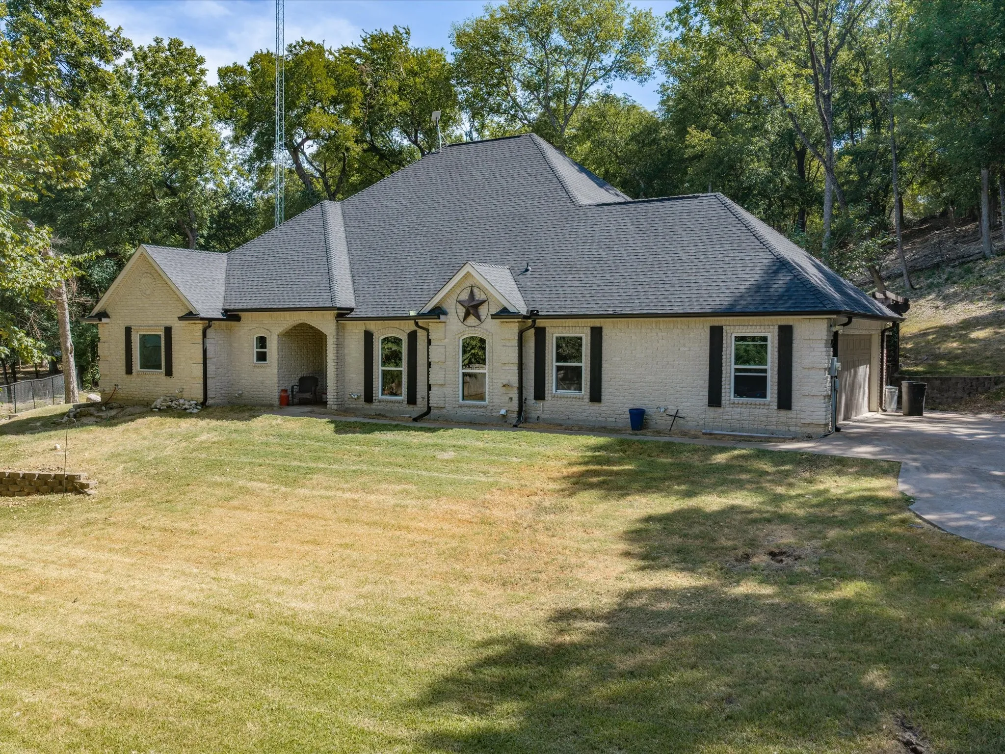 Light-toned brick exterior with dark shutters, an arched entry, and a dark shingle roof