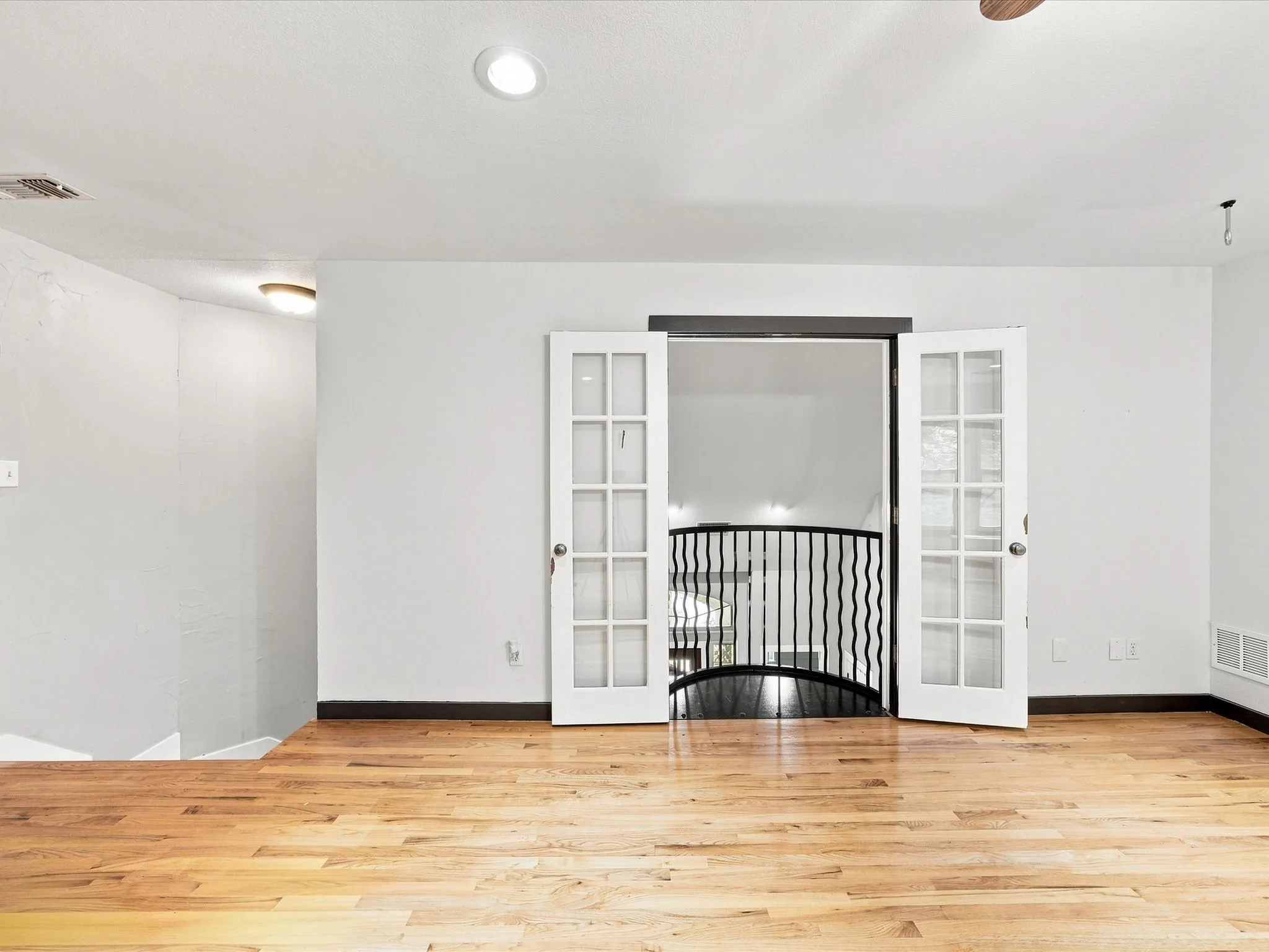 Hardwood flooring, recessed lighting, white walls, and French doors leading to a balcony with black metal railings