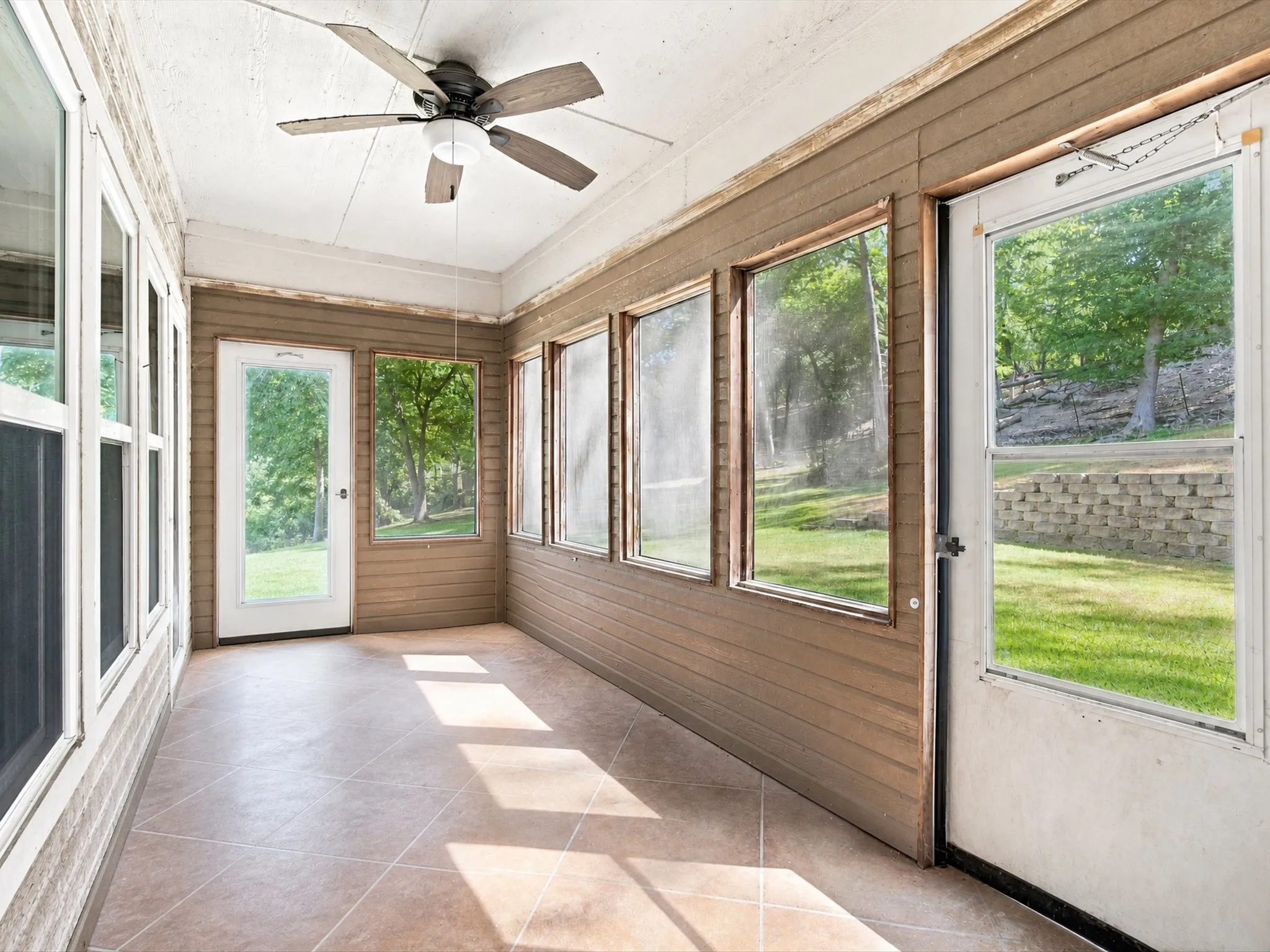 Enclosed patio featuring tile flooring, a ceiling fan, multiple windows, and a white screen door