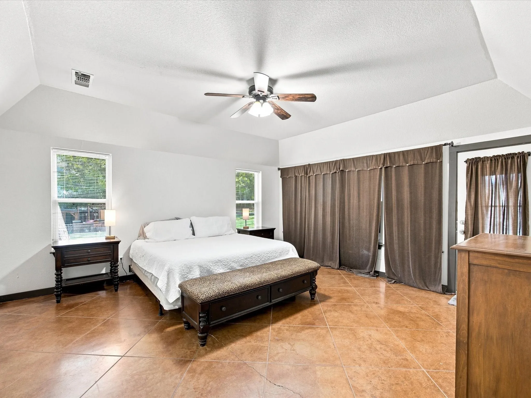 Vaulted ceiling with an integrated ceiling fan, two windows, and brown tile flooring