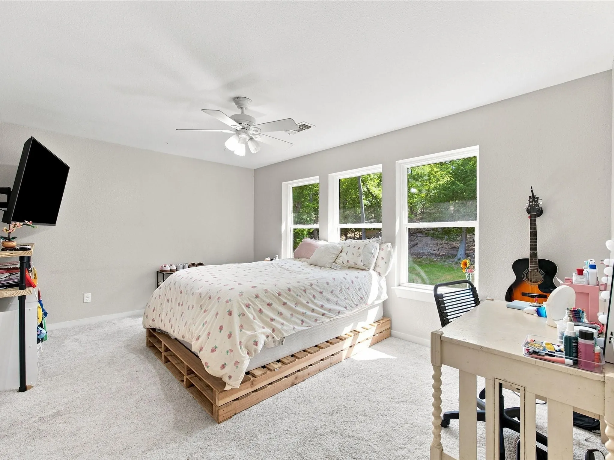 Light-colored carpeting, three windows with white frames, white ceiling fan, and light gray wall paint