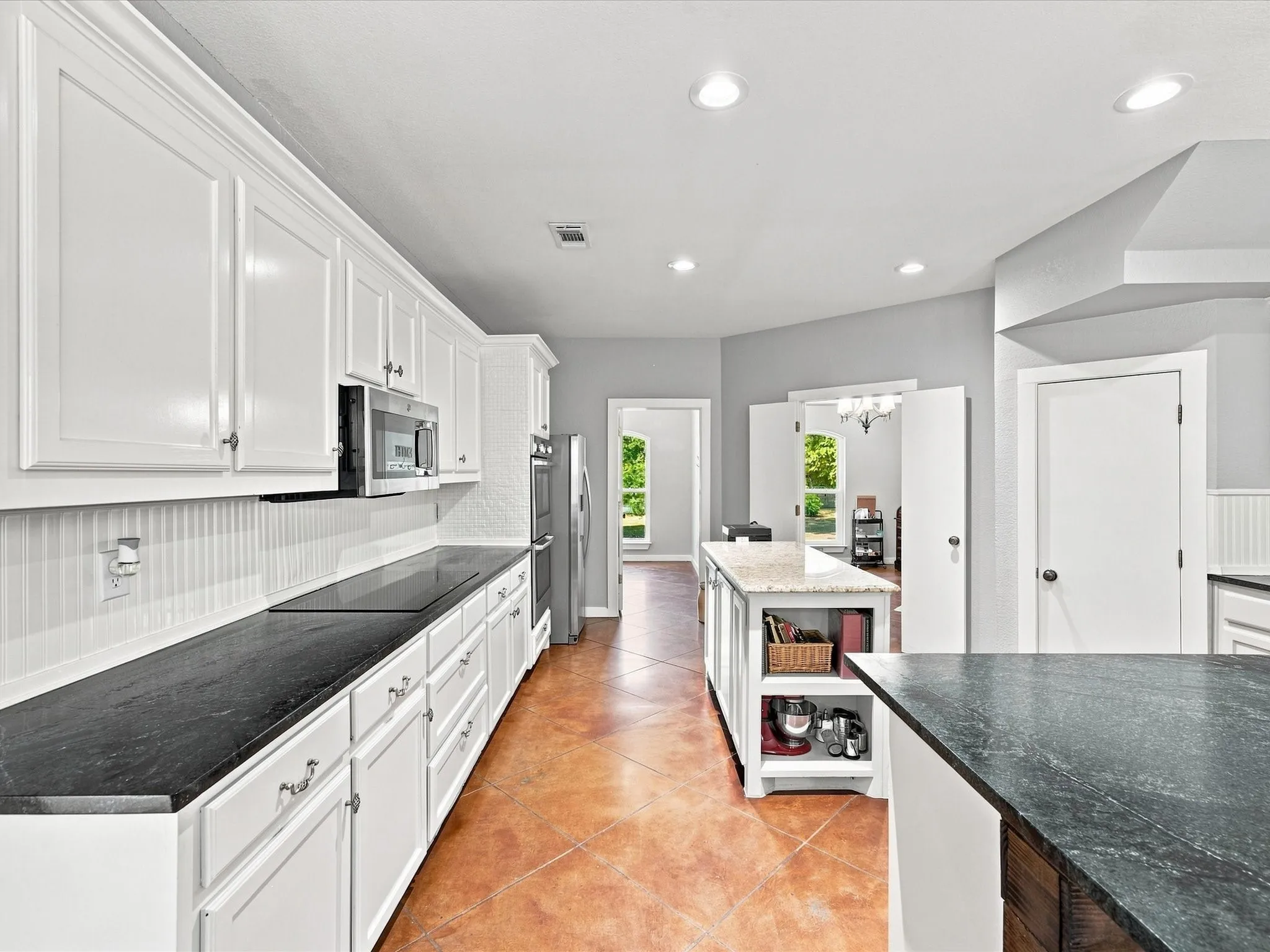 White cabinetry with crown molding, dark countertops, a central island with a lighter countertop, stainless steel appliances, and recessed lighting