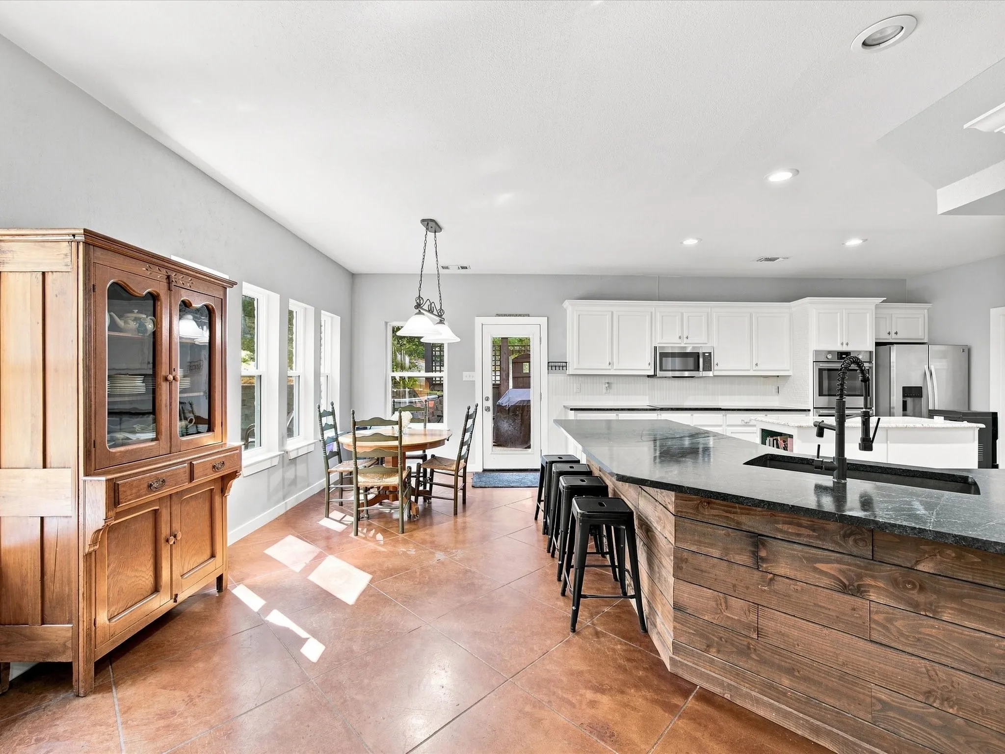 Spacious kitchen featuring an expansive island with wood paneling, dark stone countertops, white cabinetry, and stainless steel appliances