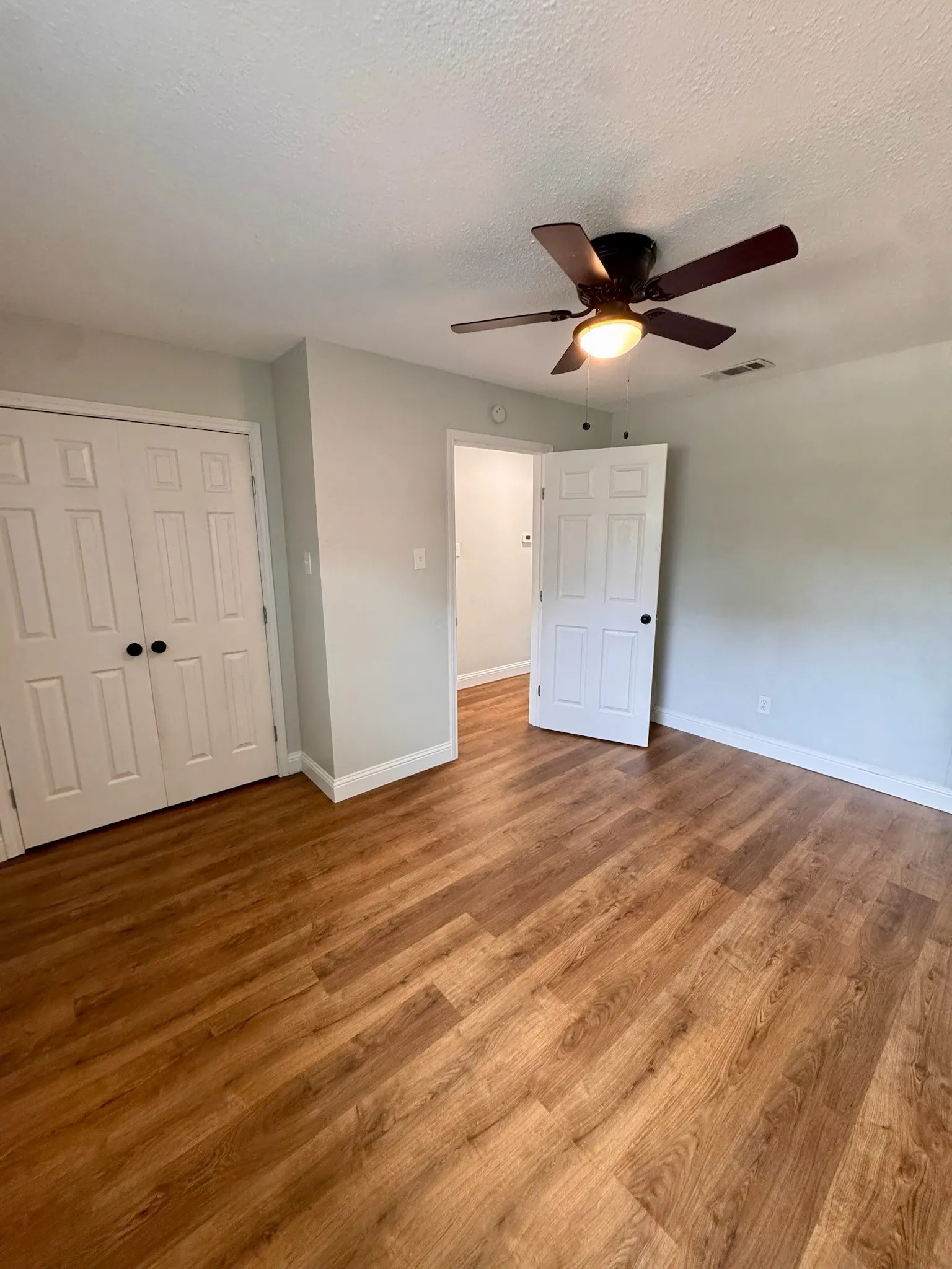 Wood-finish flooring, ceiling fan with integrated lighting, paneled doors, and light-toned wall paint