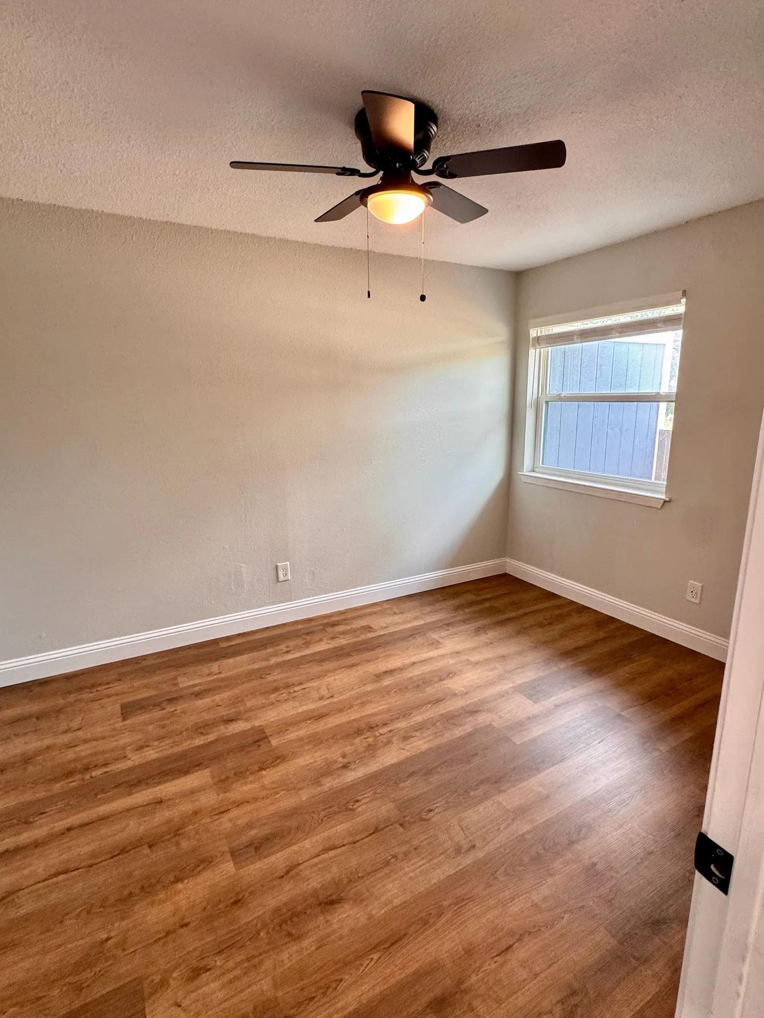Wood-finish flooring, a ceiling fan with integrated lighting, and a white-framed window