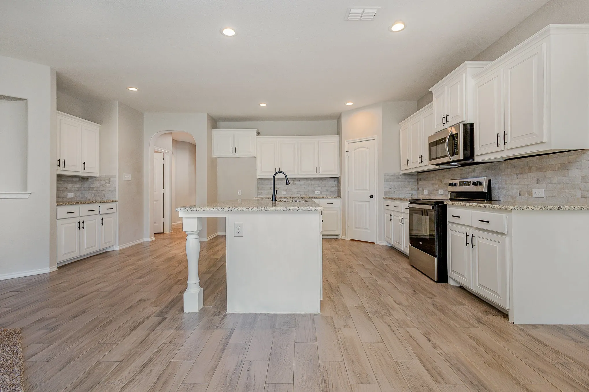 View of kitchen from living and dining area. Featuring white cabinets, large island with sink and sitting area, dry bar that may be used as coffee bar, stainless steel appliances
