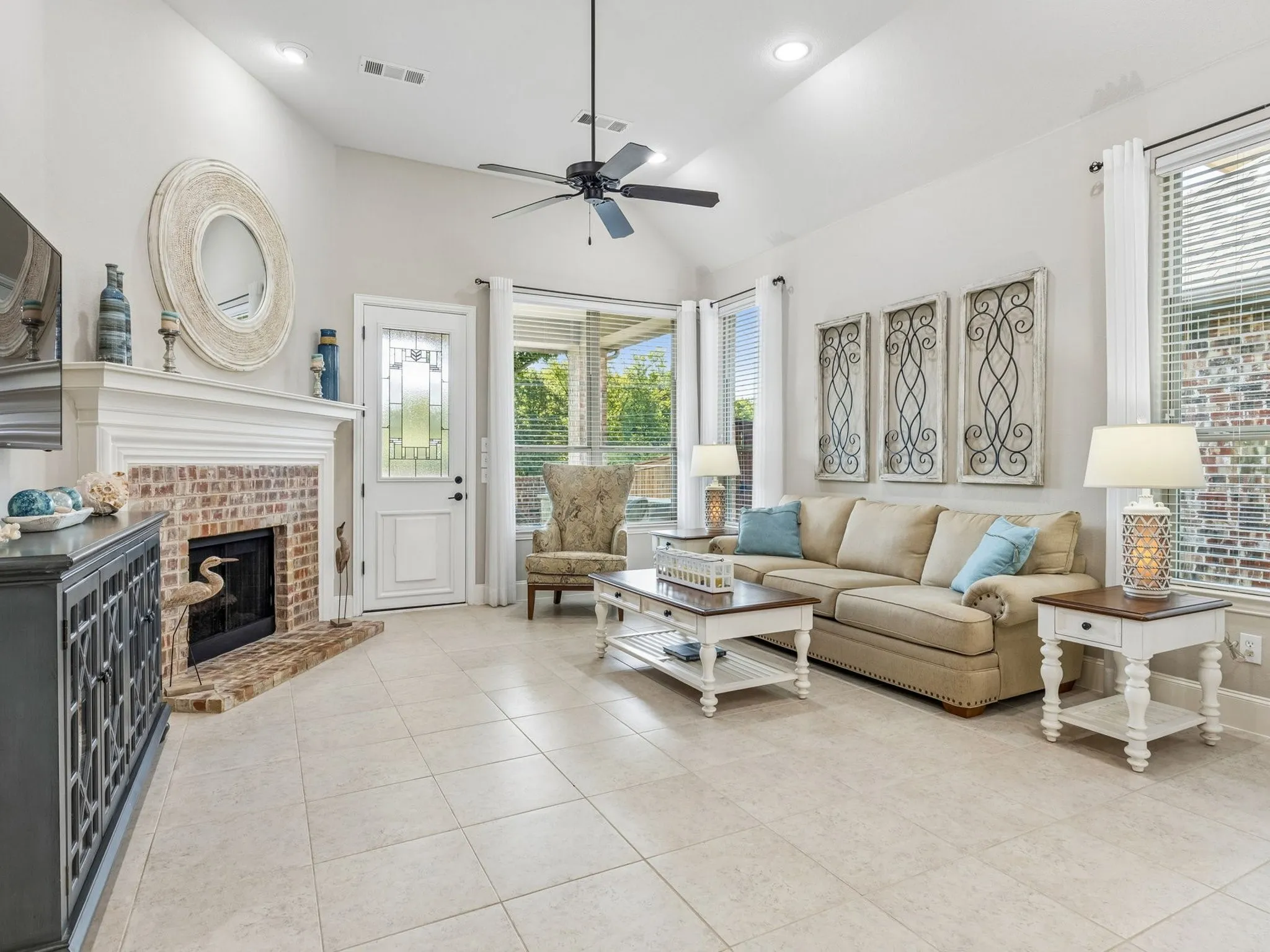 Vaulted ceiling with recessed lighting and a ceiling fan, tiled flooring, brick fireplace with a white mantel.