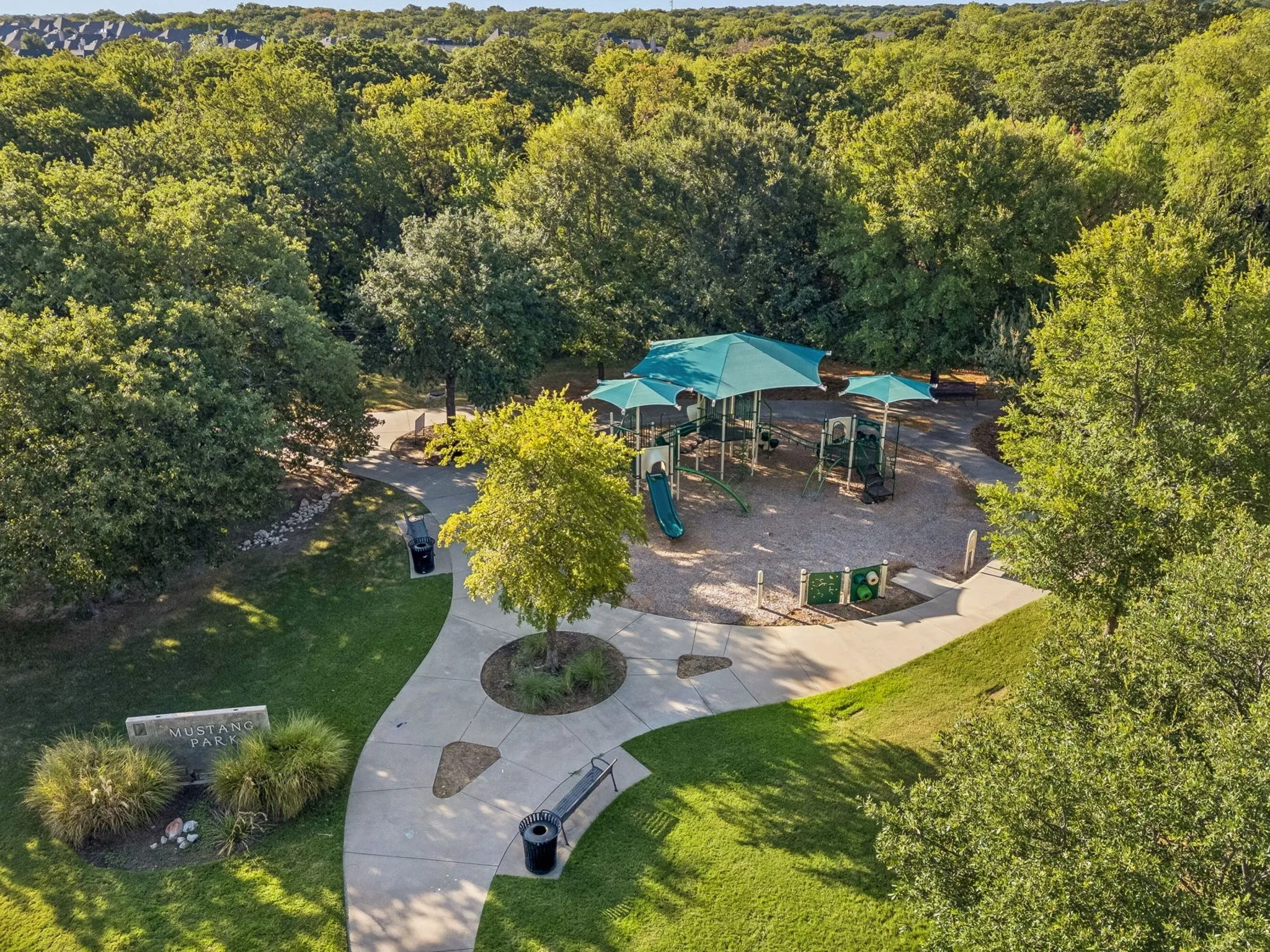 Community park with playground, shaded play structures, curved pathways, and abundant mature trees