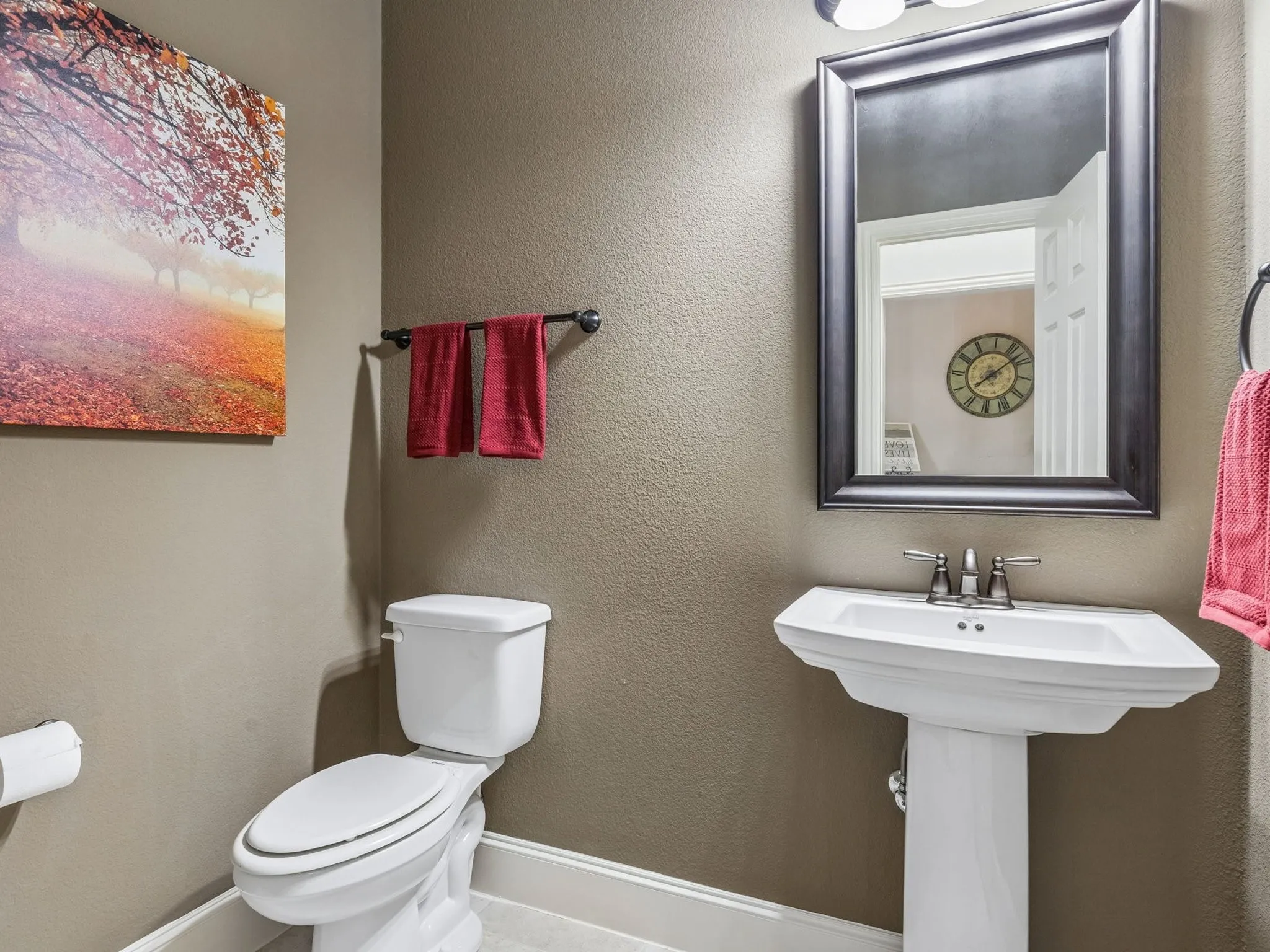 Pedestal sink with a two-handle faucet, framed mirror, and built-in toilet.