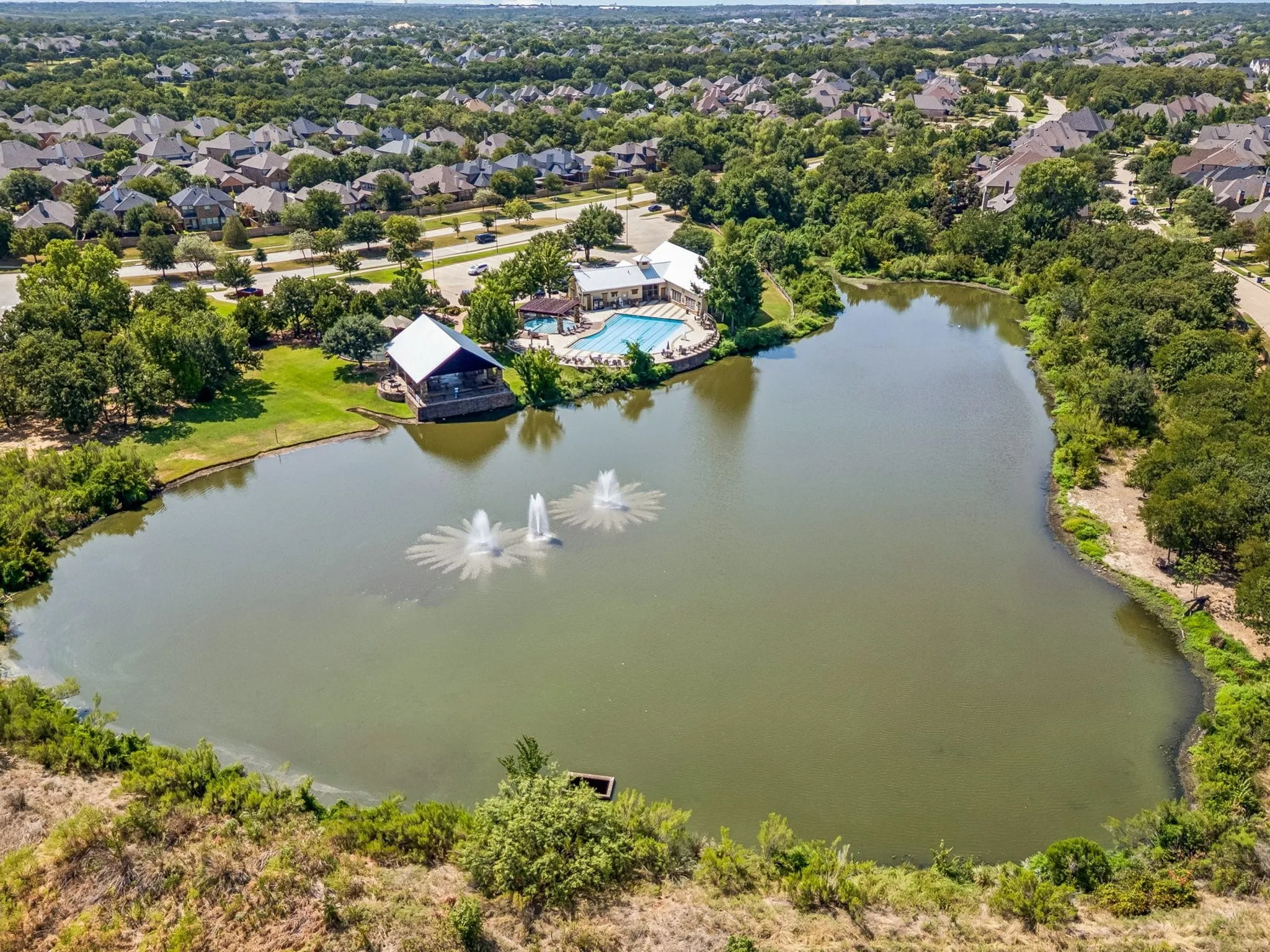 Community pond featuring two fountains, a clubhouse, and an outdoor swimming pool