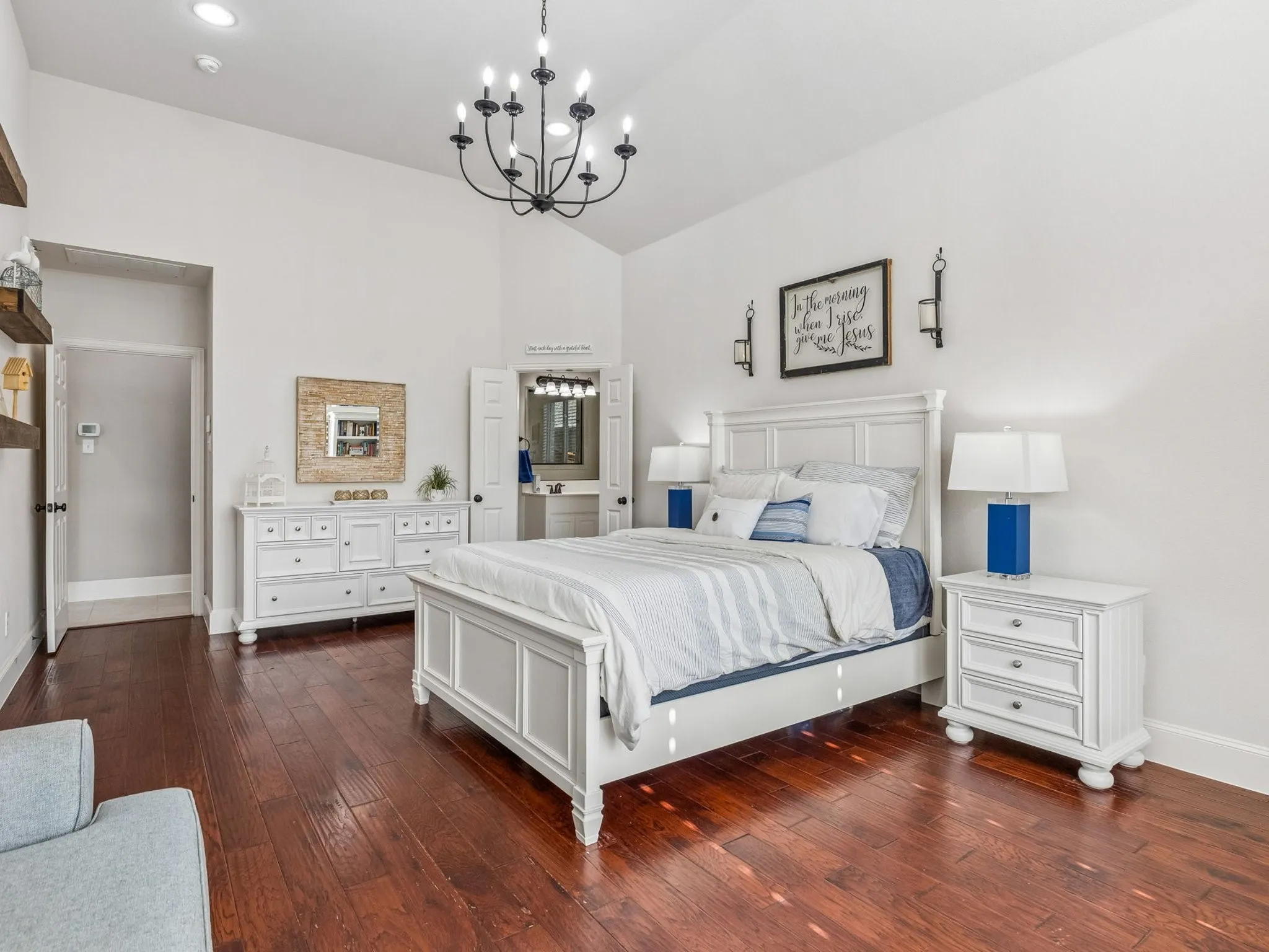 Vaulted ceiling with a chandelier, engineered hardwood-finish, and white paneled doors to primary bath.
