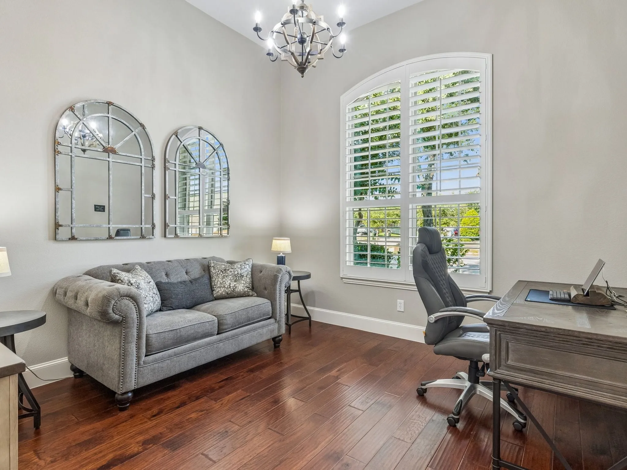 High ceilings with a chandelier, engineered hard wood flooring, a large arched window with plantation shutters, and light-toned walls.