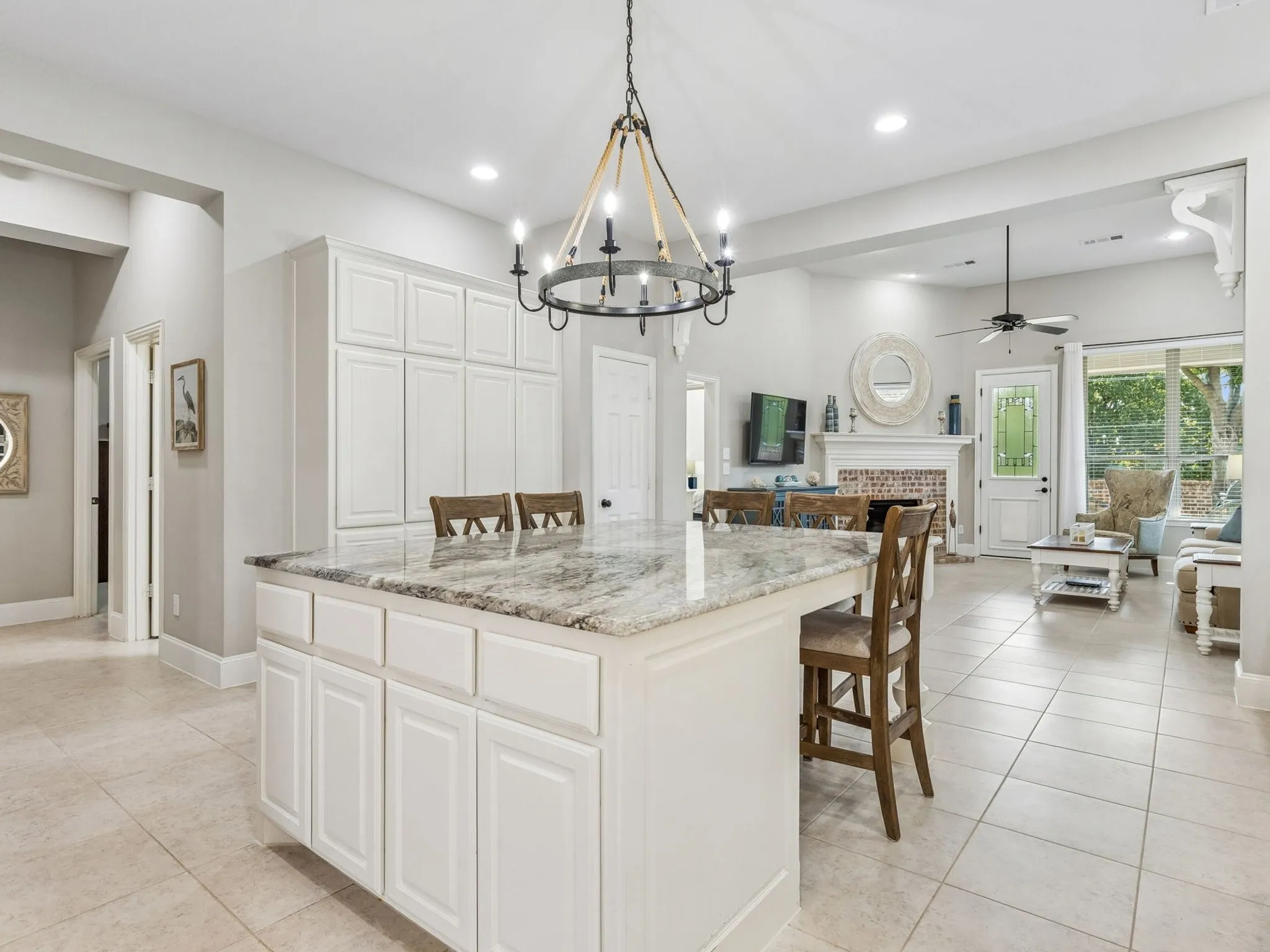 Kitchen island with granite countertop, under island storage, tile flooring, and a decorative chandelier.