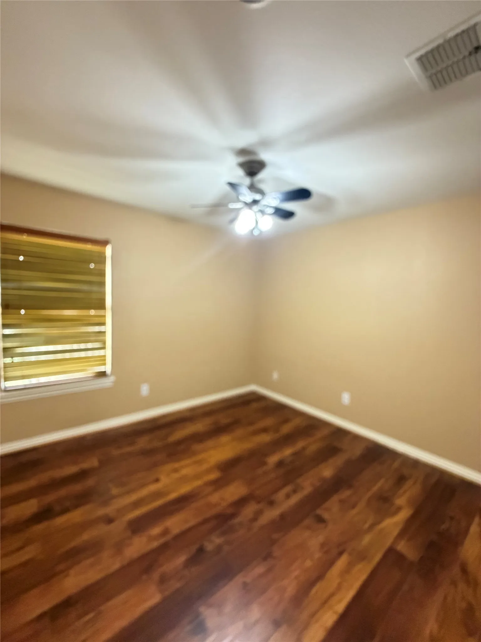 Wood-finish flooring with baseboard trim, neutral wall paint, and a ceiling fan with integrated lighting