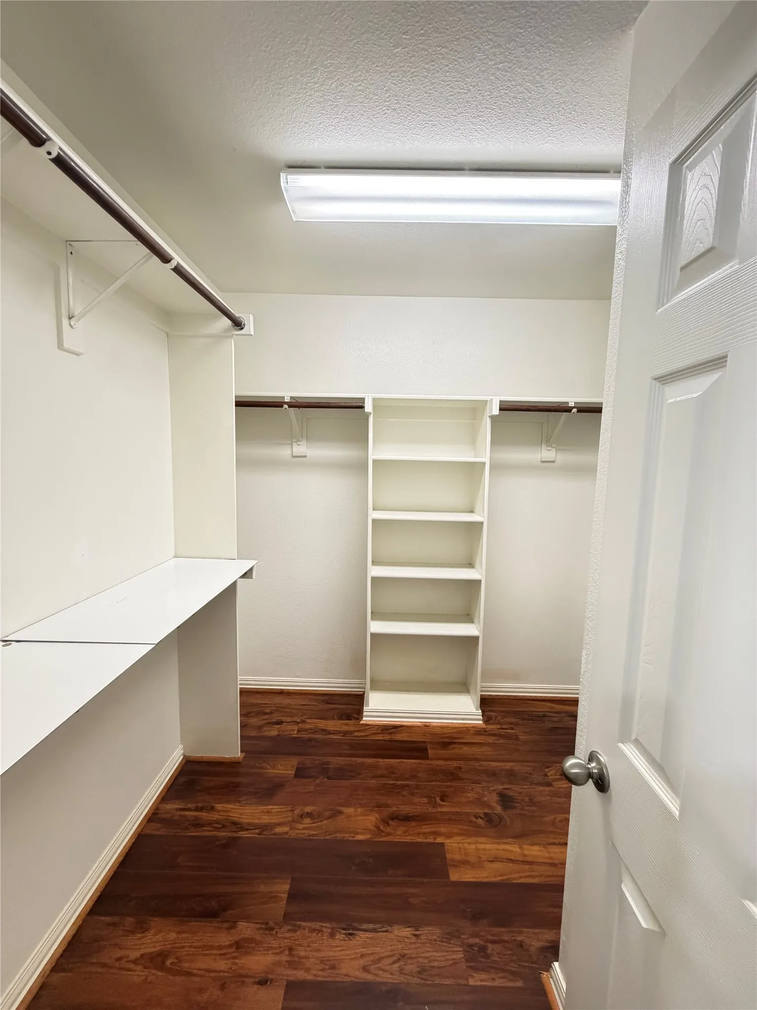 Spacious walk-in closet featuring wood-finish flooring and built-in shelving