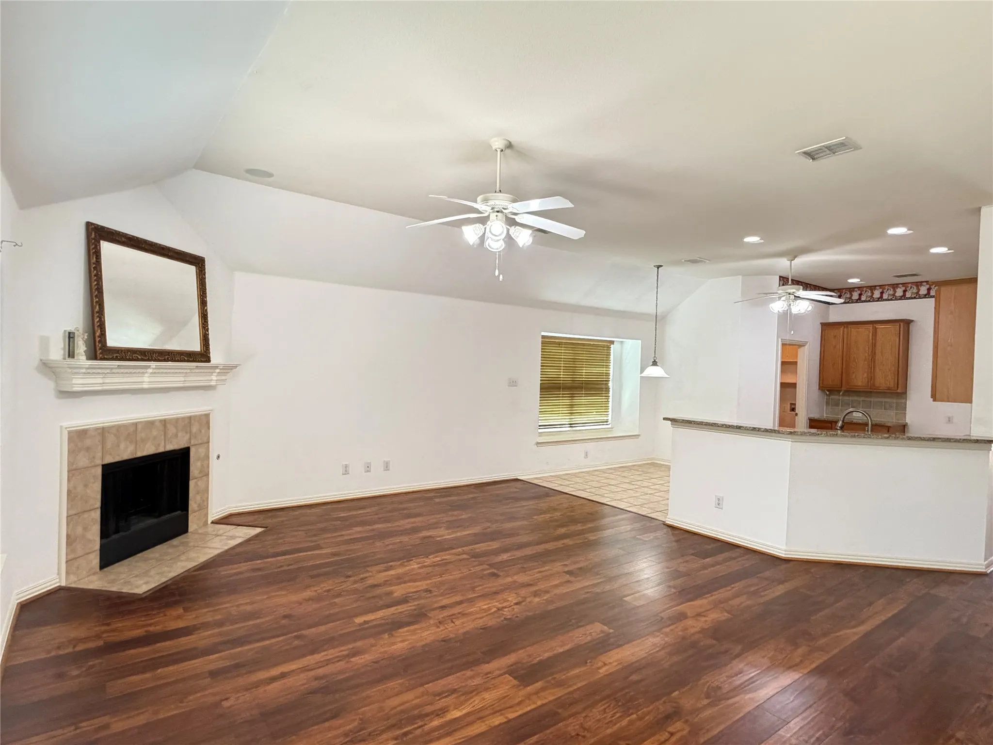 Vaulted ceiling, wood-finish flooring, fireplace with tile surround, kitchen pass-through with granite-look countertop, and wood cabinetry