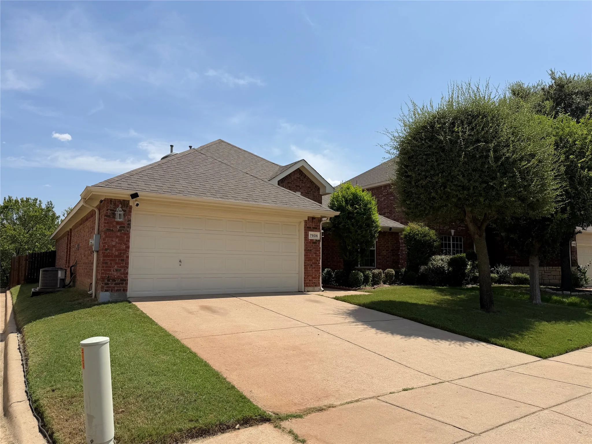 Brick exterior, attached two-car garage, concrete driveway, mature trees, and established landscaping