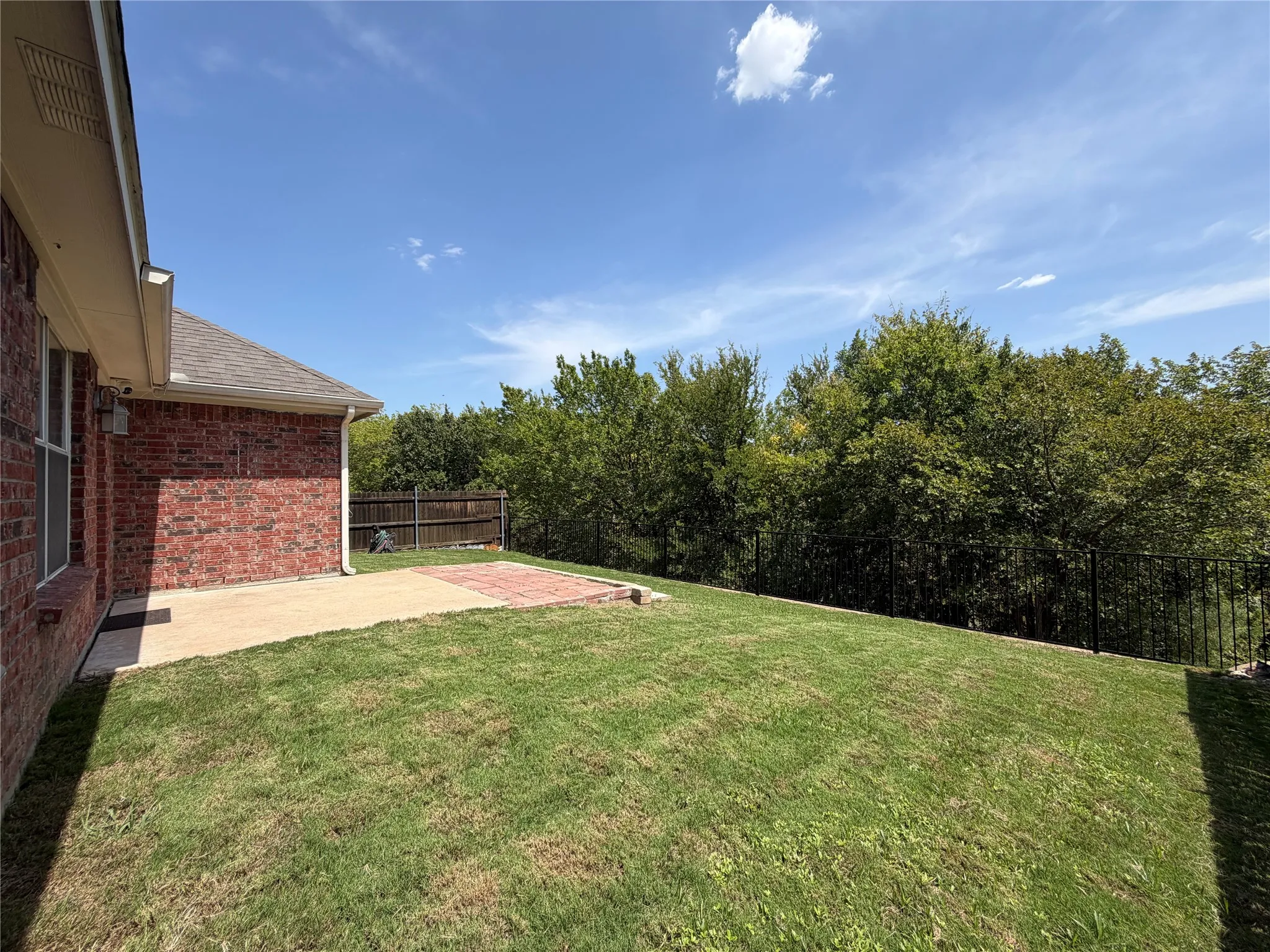 Expansive backyard featuring a manicured lawn, brick paver patio, concrete patio, and a black wrought iron fence