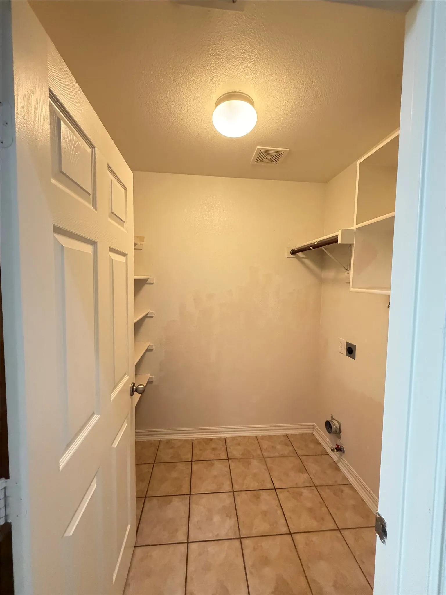 Utility room with ceramic tile flooring, built-in shelving, a clothes rod, and an overhead flush-mount light fixture