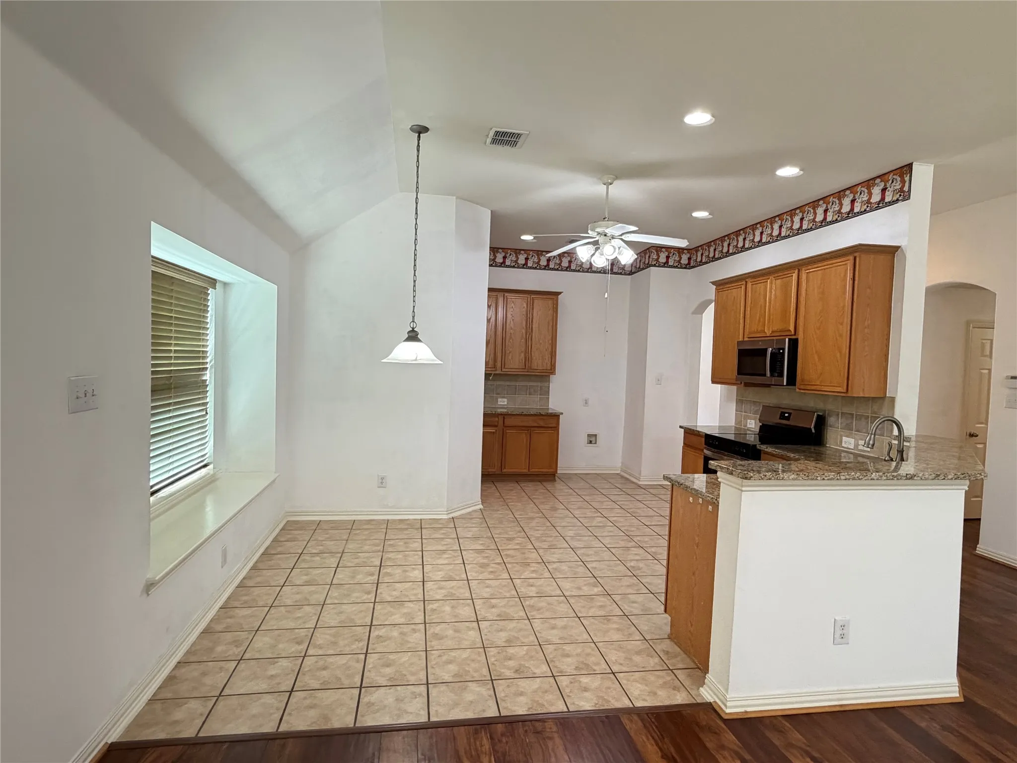 Kitchen with wood cabinetry, granite countertops, tile backsplash, stainless steel appliances, and tile flooring