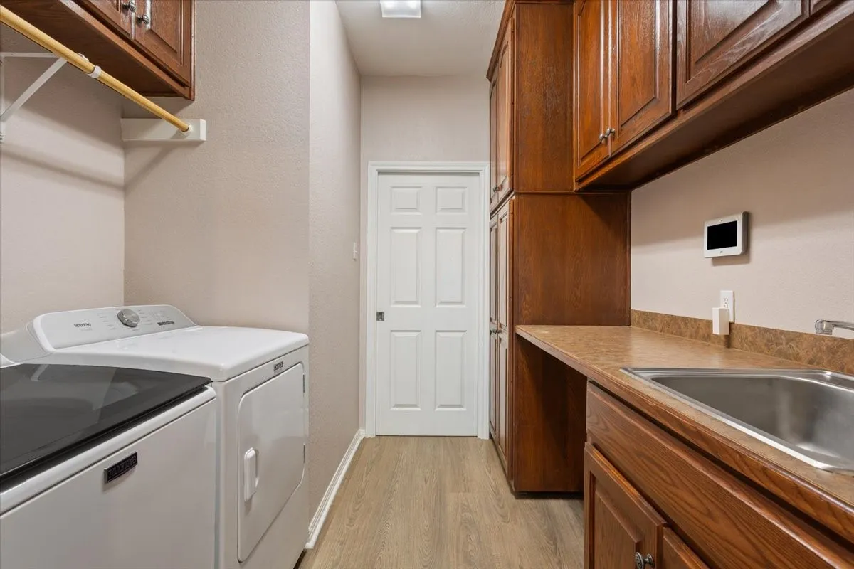 Laundry room featuring wood-finish flooring, ample cabinetry, and a utility sink