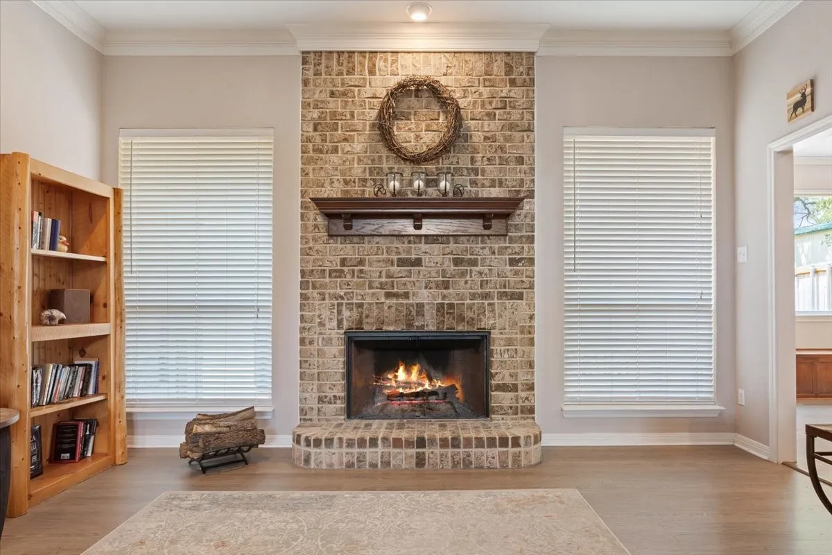Brick fireplace with a wood mantel, crown molding, and wood-finish flooring