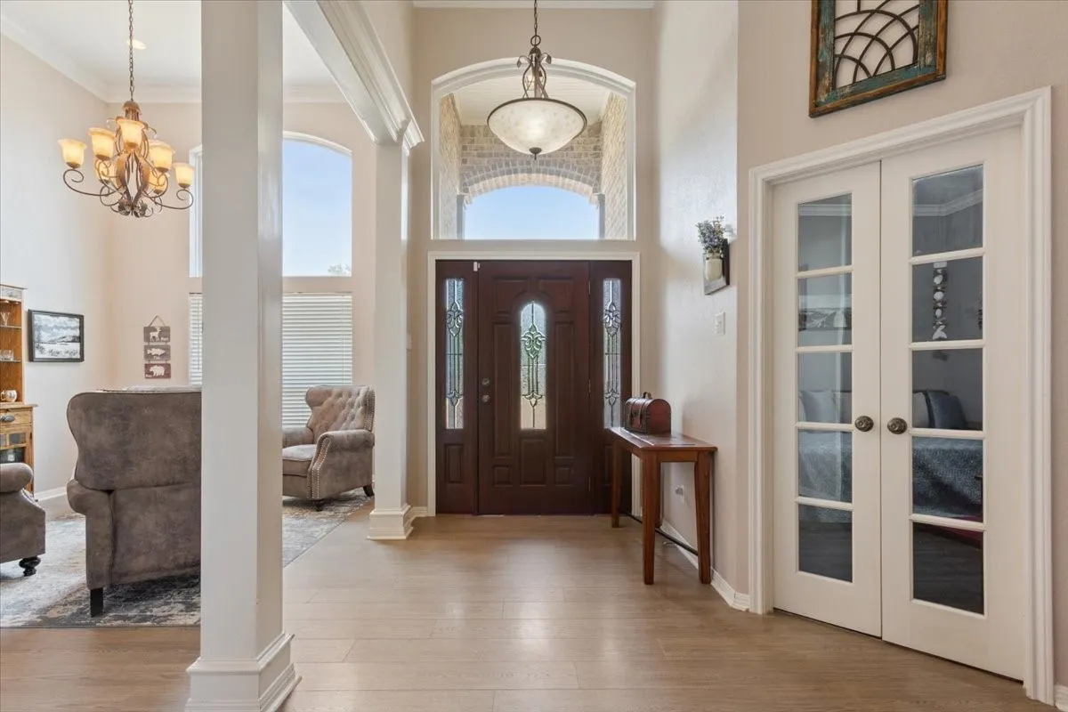 Wood-finish flooring, white paneled French doors, vaulted ceiling, decorative chandelier, and an ornate front door with leaded glass