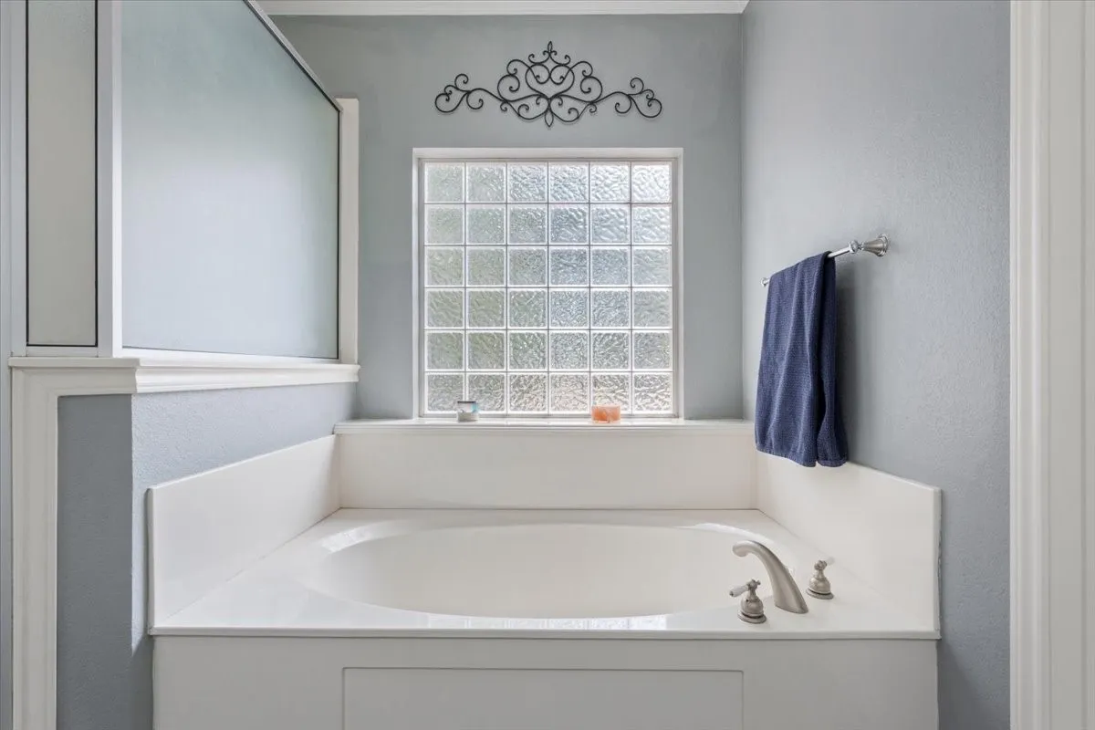 Built-in soaking tub with brushed nickel fixtures, glass block window, and frosted glass shower enclosure