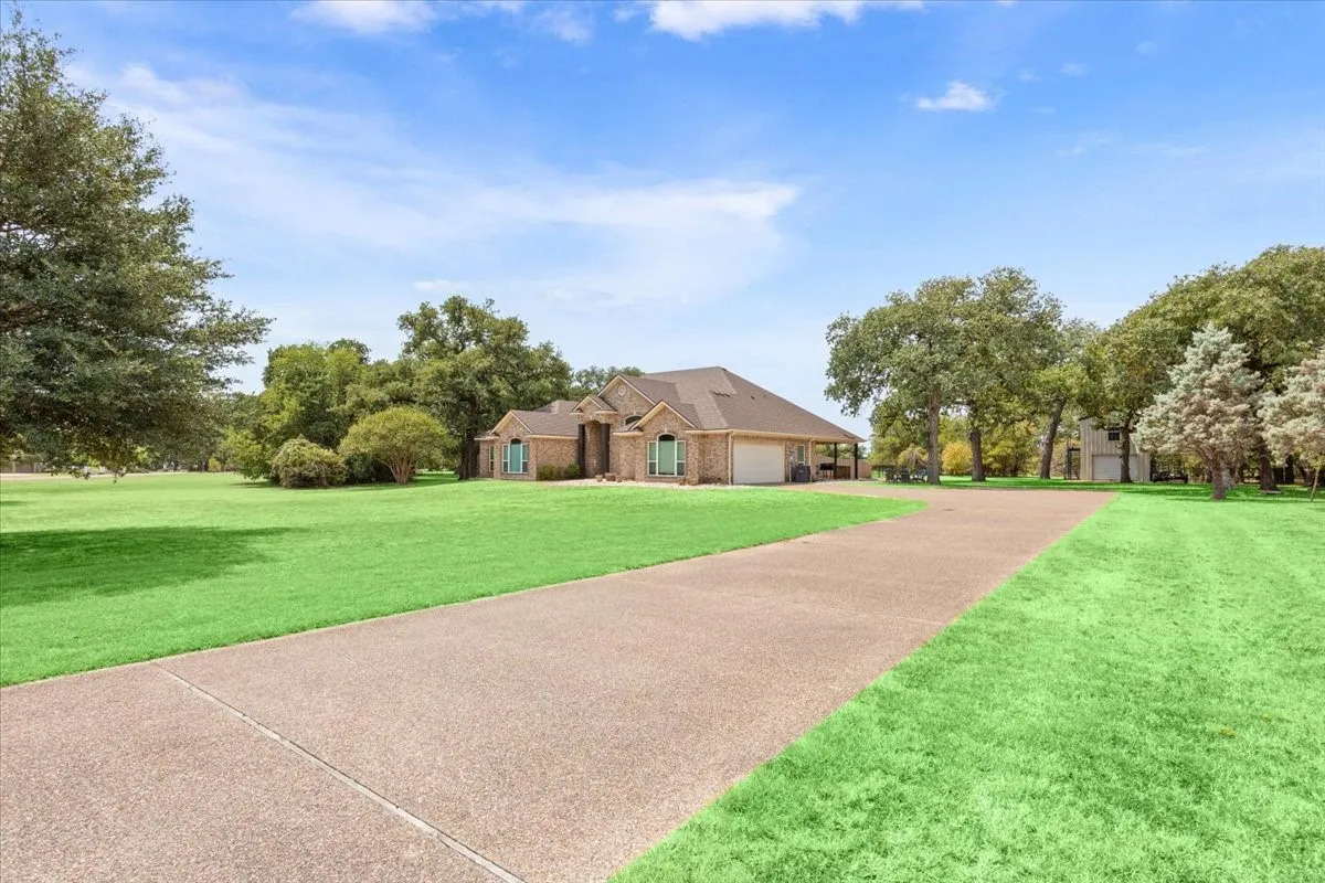 Brick exterior with a multi-car garage, expansive lawn, mature trees, and a paved driveway