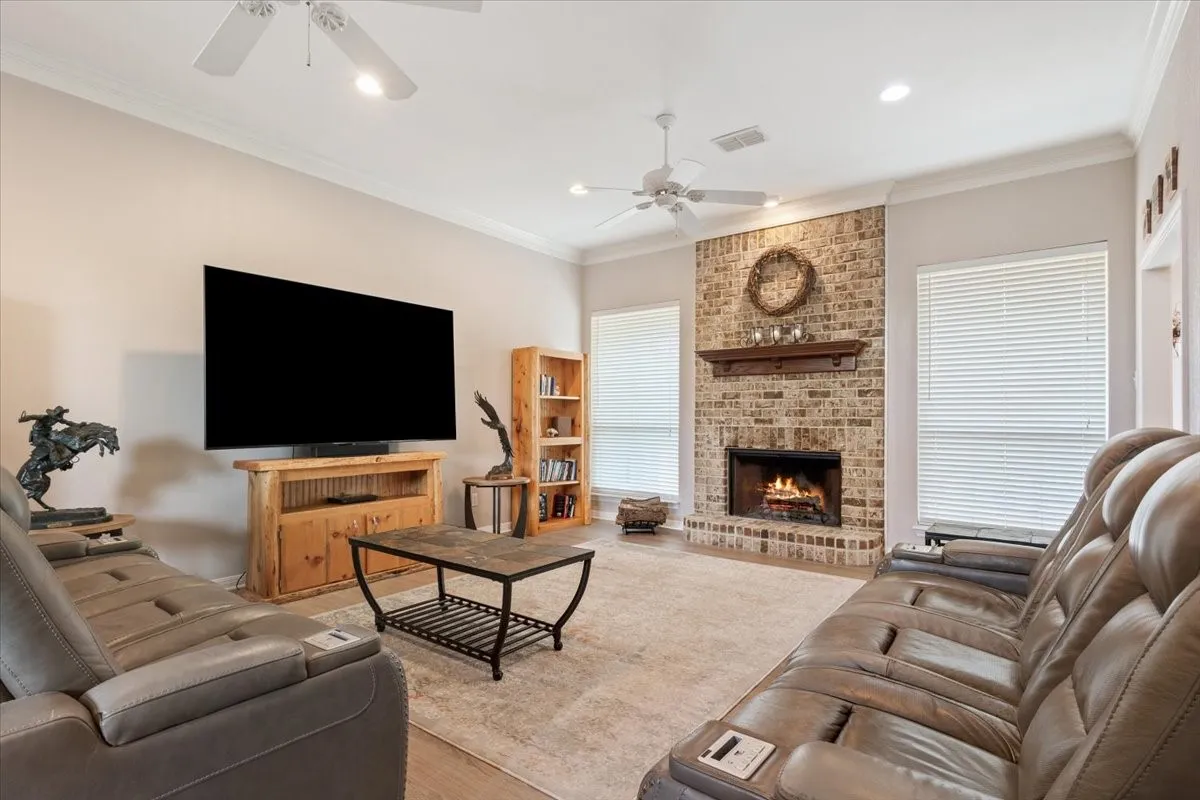 Brick fireplace with a wood mantle, crown molding, ceiling fans, and wood-finish flooring
