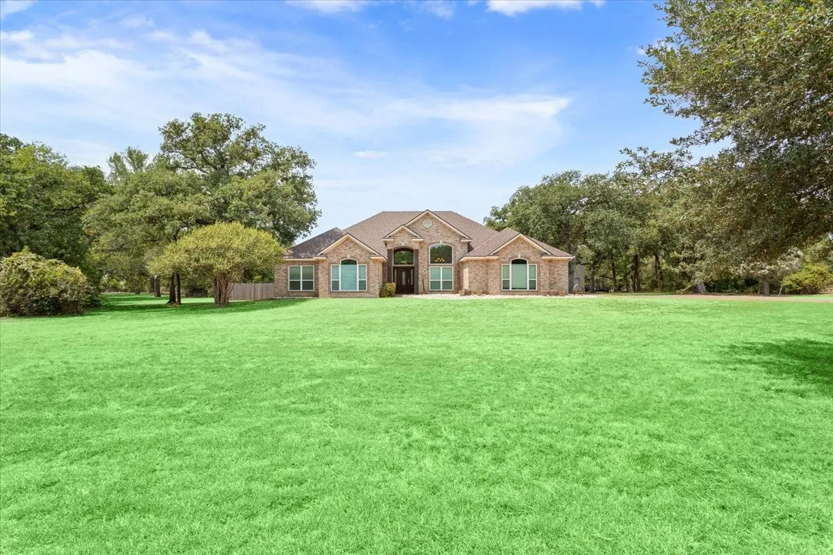 Brick exterior residence with a prominent arched entry, surrounded by mature trees and a vast green lawn