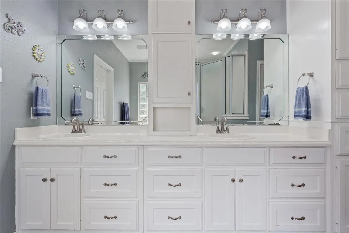 Dual vanity with integrated sinks, expansive countertop, white cabinetry with silver-tone hardware, and two framed mirrors with overhead lighting