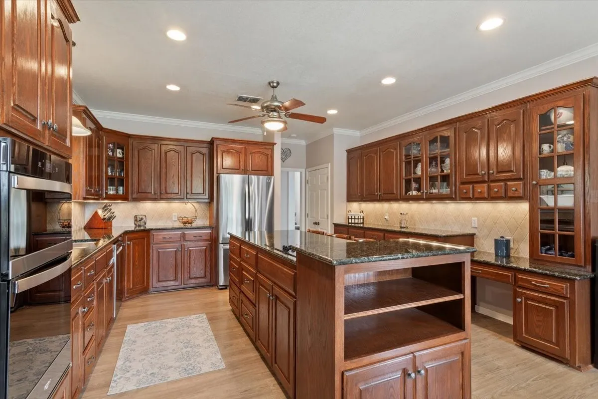 Kitchen featuring extensive wood cabinetry, dark countertops, stainless steel appliances, and wood-finish flooring