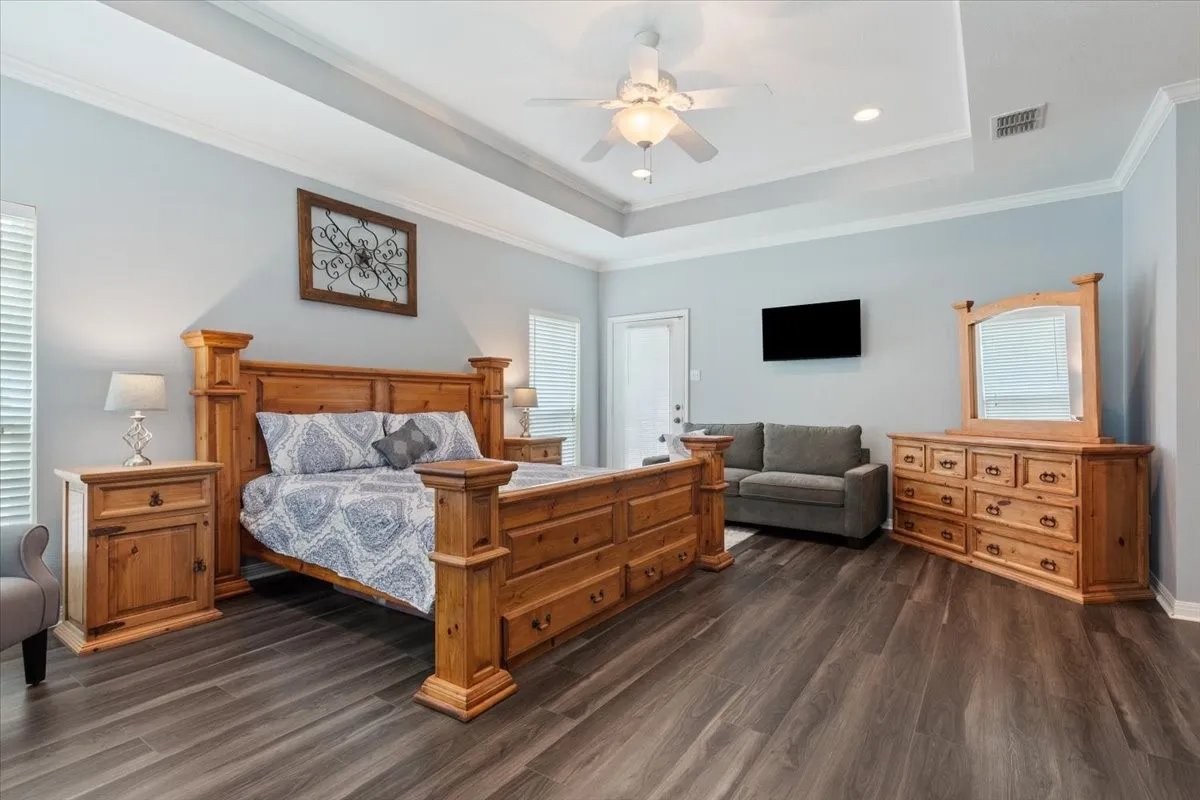 Wood-finish flooring, tray ceiling, recessed lighting, ceiling fan, and crown molding