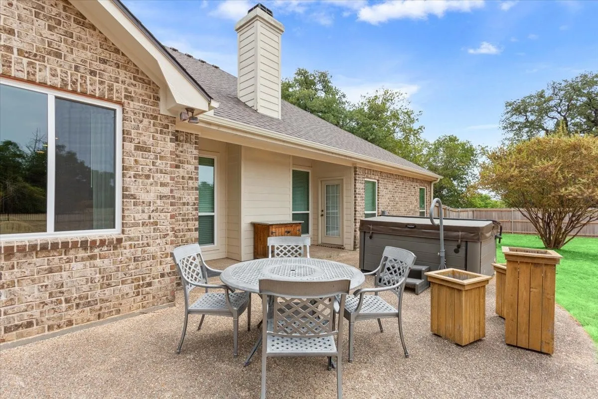 Expansive patio with a concrete surface, featuring a built-in hot tub, brick exterior, and a manicured lawn