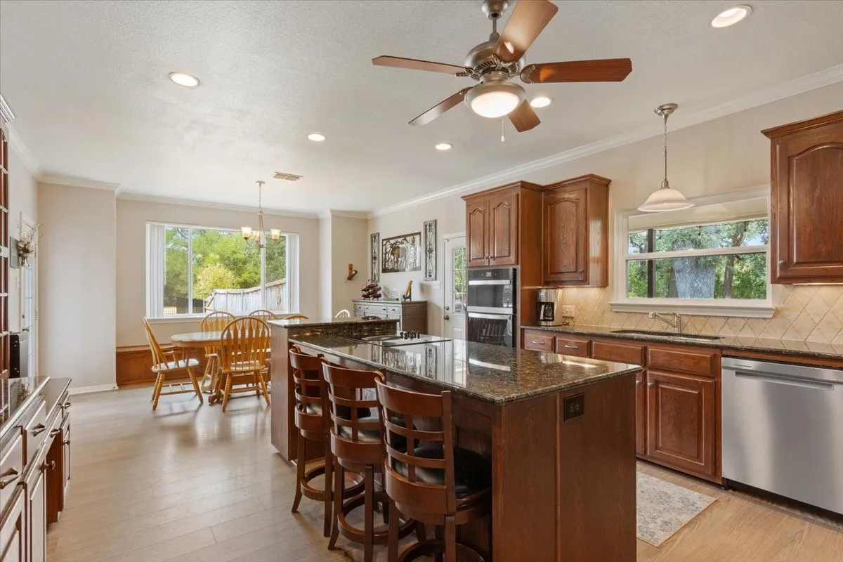 Spacious kitchen featuring an expansive center island with seating, dark wood cabinetry, stainless steel appliances, and wood-finish flooring