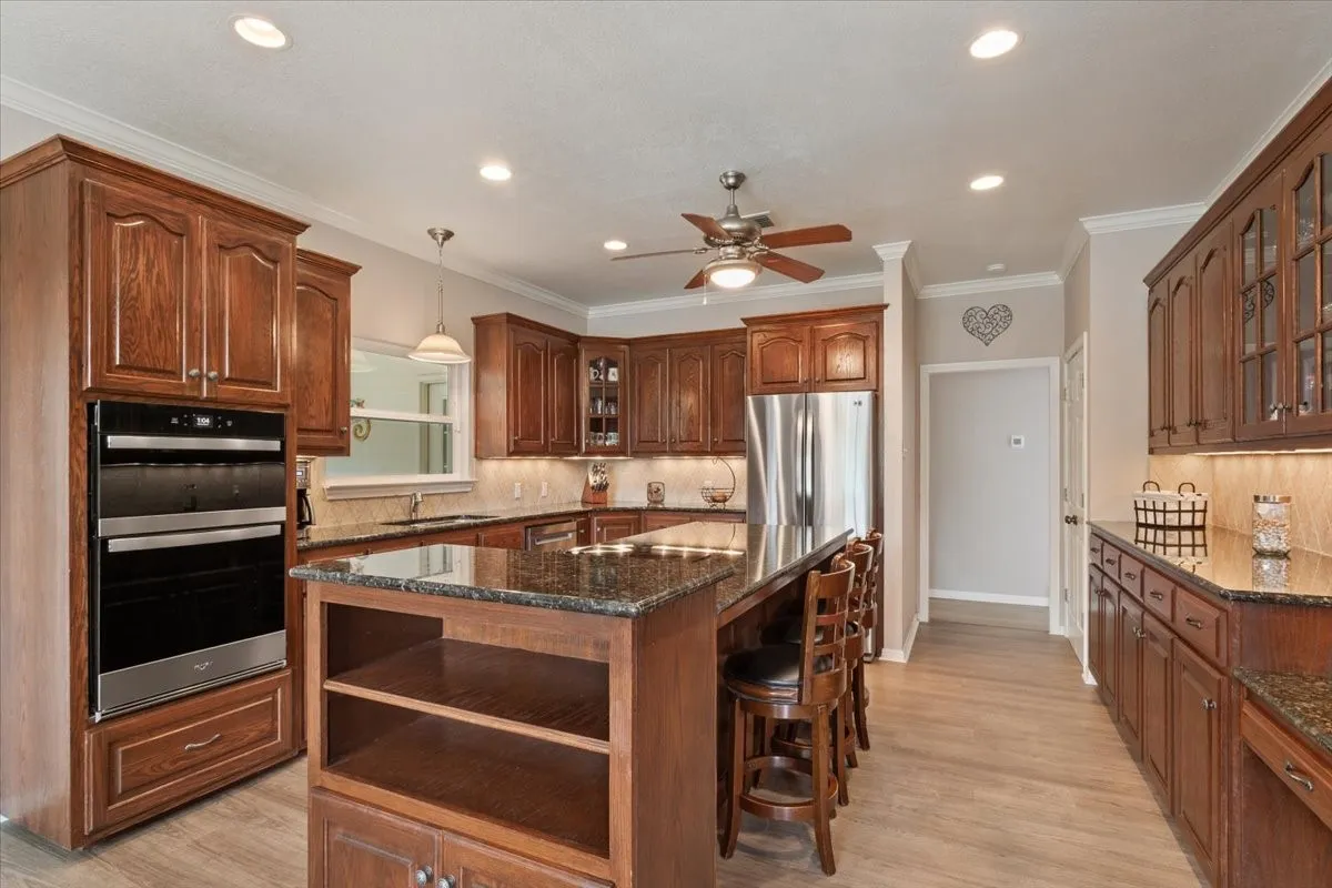 Expansive kitchen featuring wood-finish cabinetry, granite countertops, stainless steel appliances, a built-in double oven, and recessed lighting