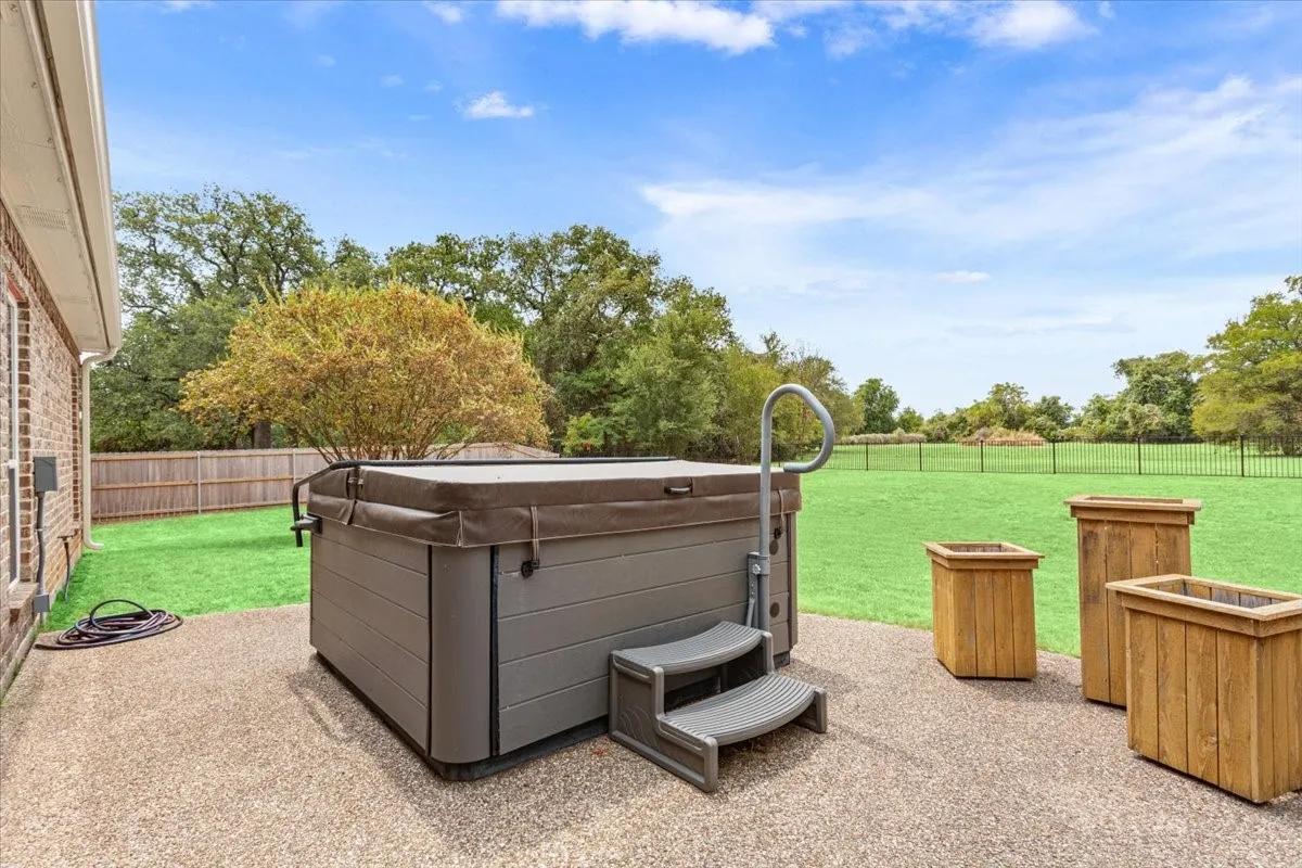 Expansive outdoor patio featuring a hot tub with steps, a metal handrail, and a surrounding lawn