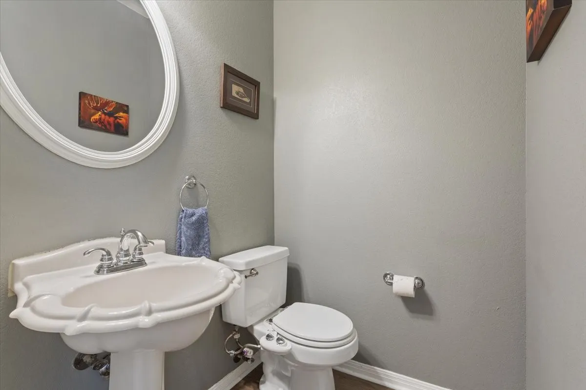 Pedestal sink with chrome-finish faucet, oval mirror, and a white toilet