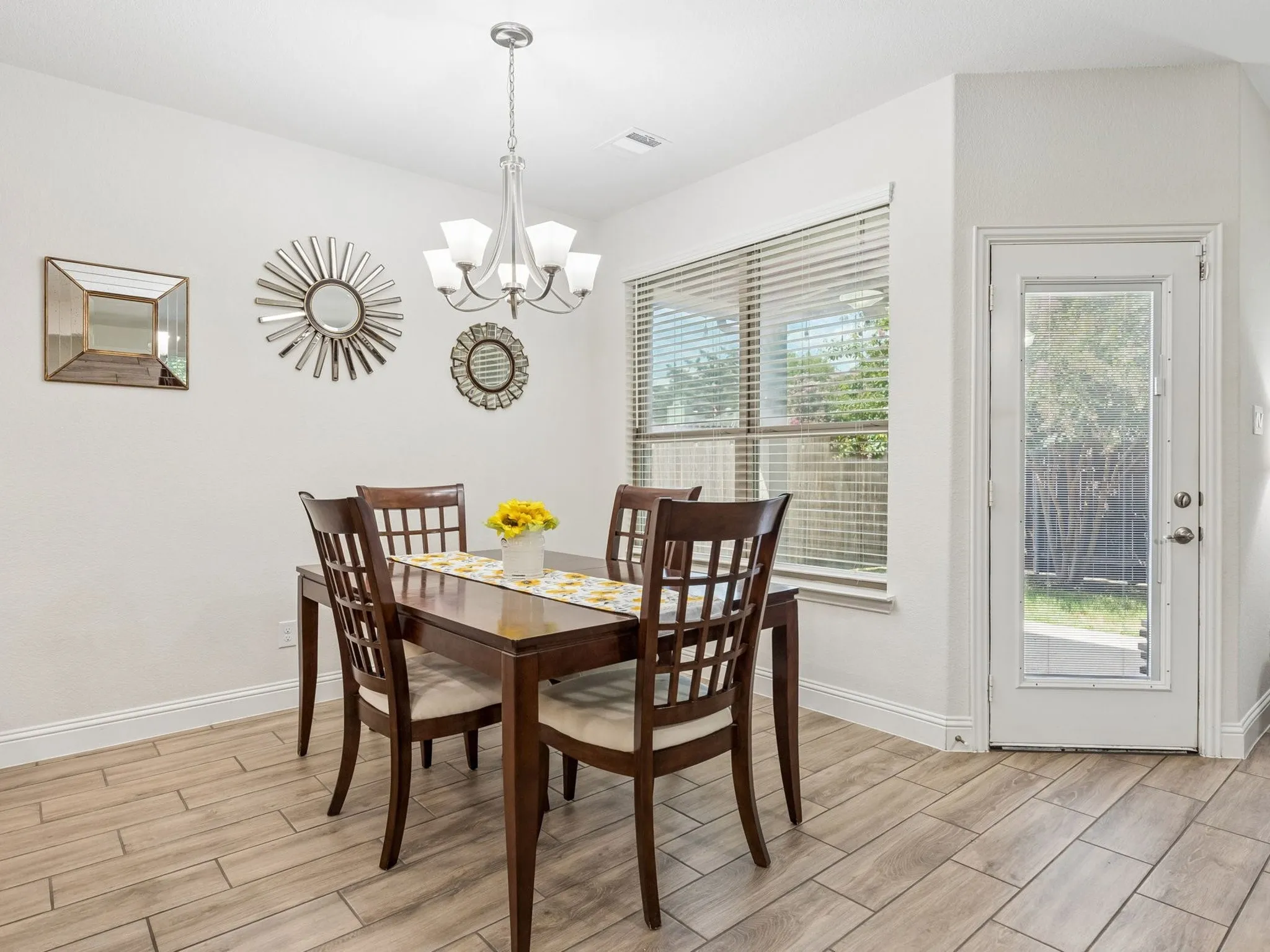 Wood-finish tile flooring, overhead chandelier, large window with blinds, and white trim