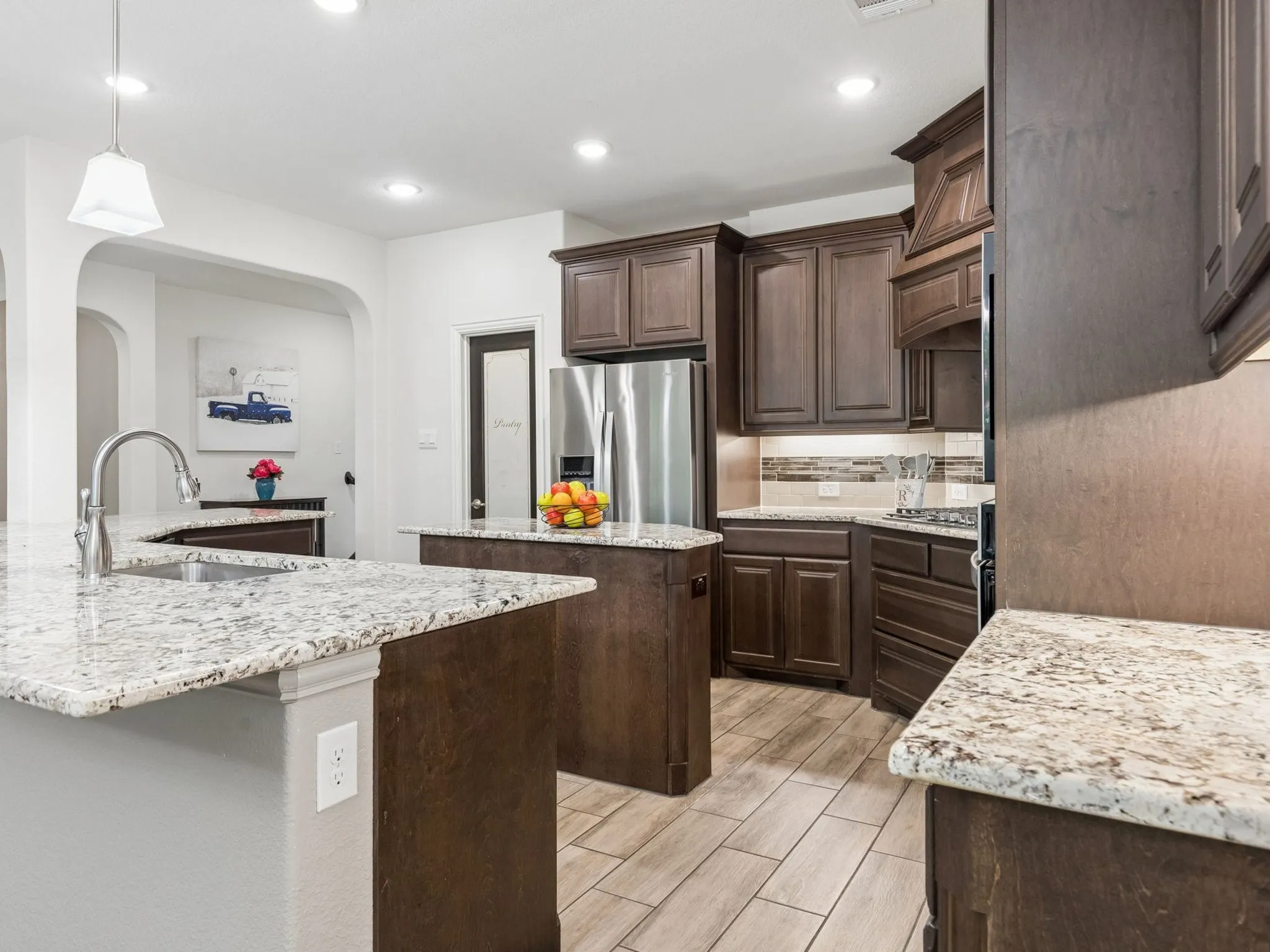 Kitchen featuring wood-finish tile flooring, dark wood cabinetry, stainless steel appliances, granite countertops, and a tile backsplash
