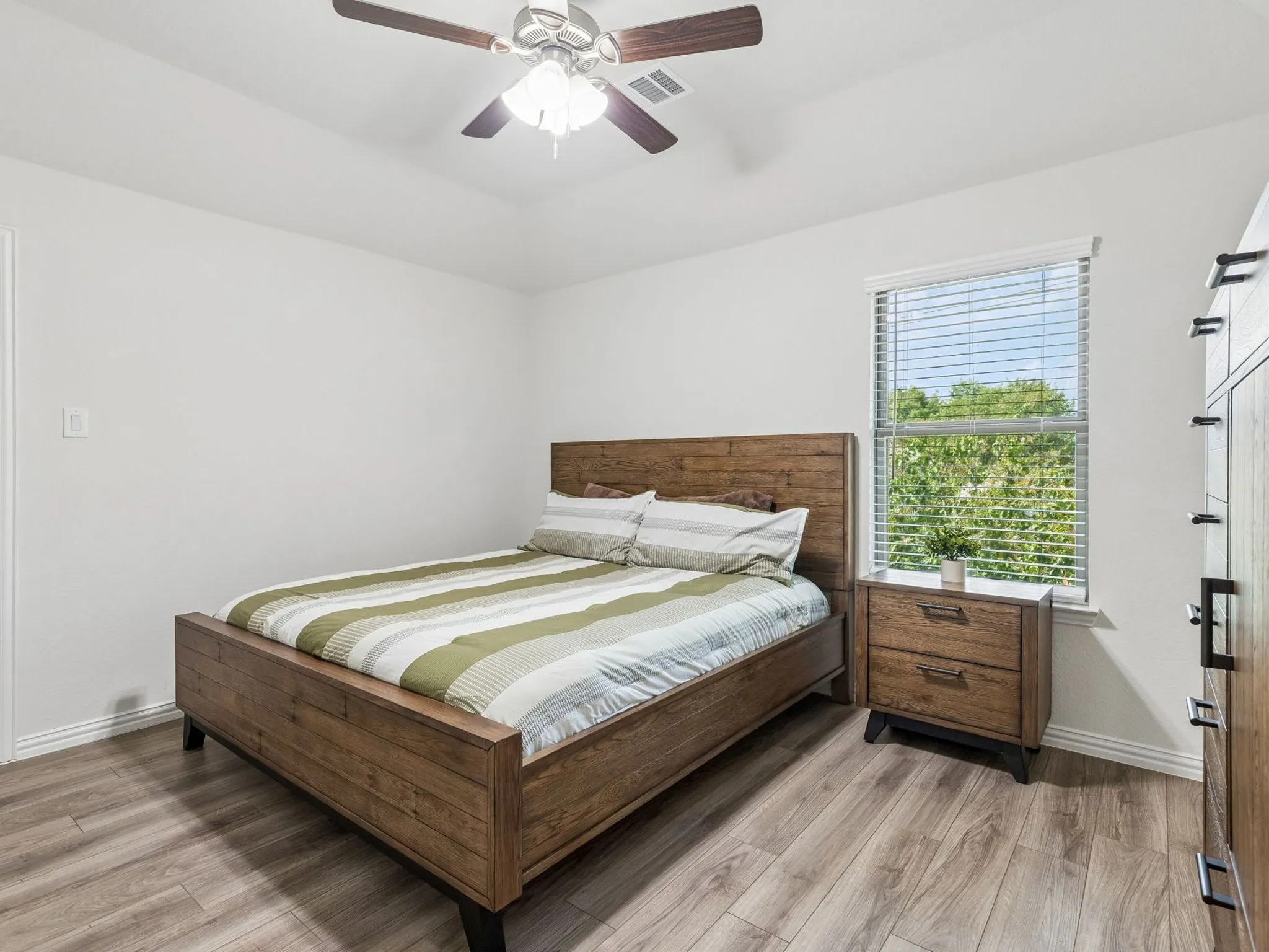 Wood-finish LVP flooring, ceiling fan with integrated lighting, window with blinds, and light wall finishes