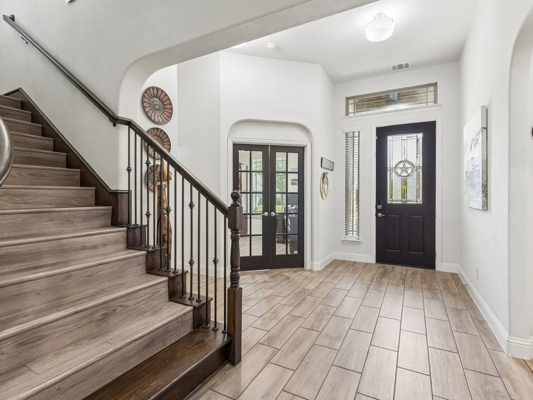 Wood-finish staircase with wrought iron balusters, dark wood handrail, and tile flooring