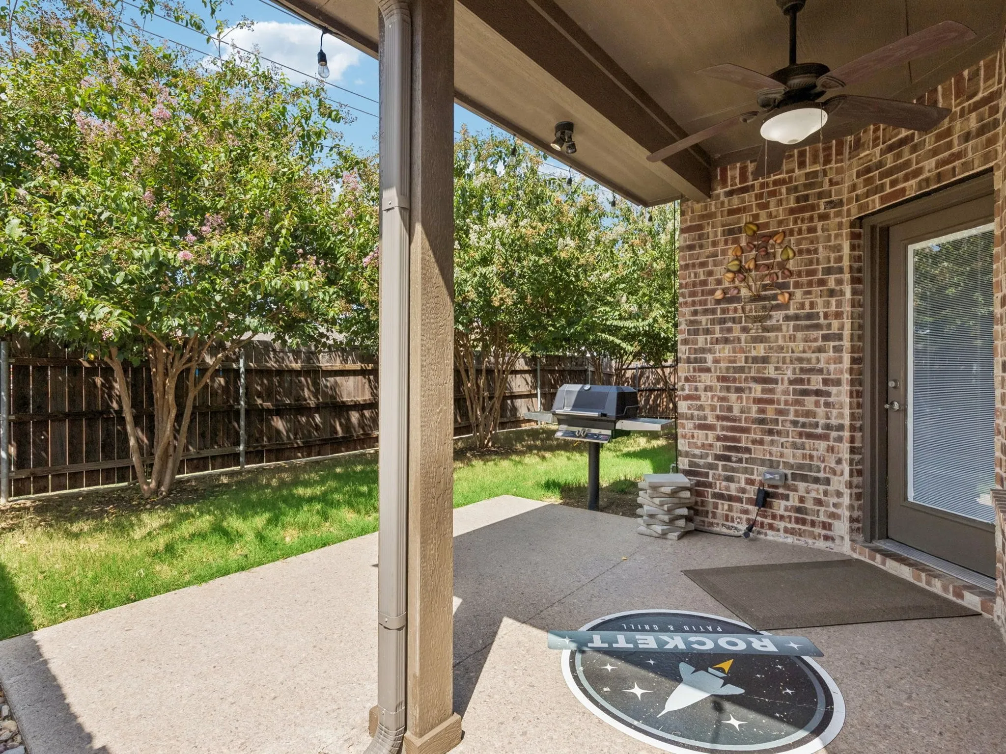 Covered patio with a ceiling fan, brick exterior wall, and privacy fencing