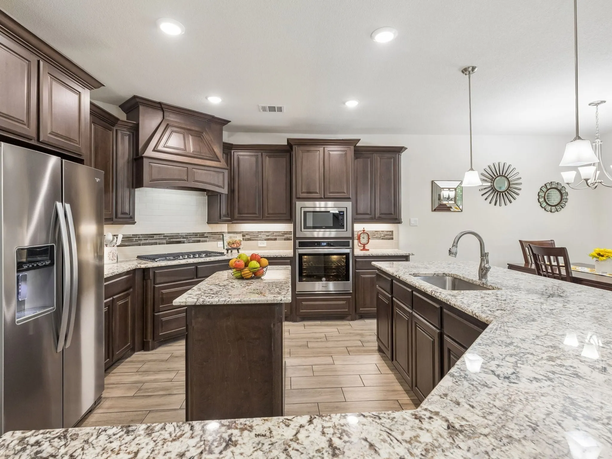Chef's kitchen featuring dark wood cabinetry with raised-panel doors, stainless steel appliances including dual wall ovens, gas cooktop, and side-by-side refrigerator