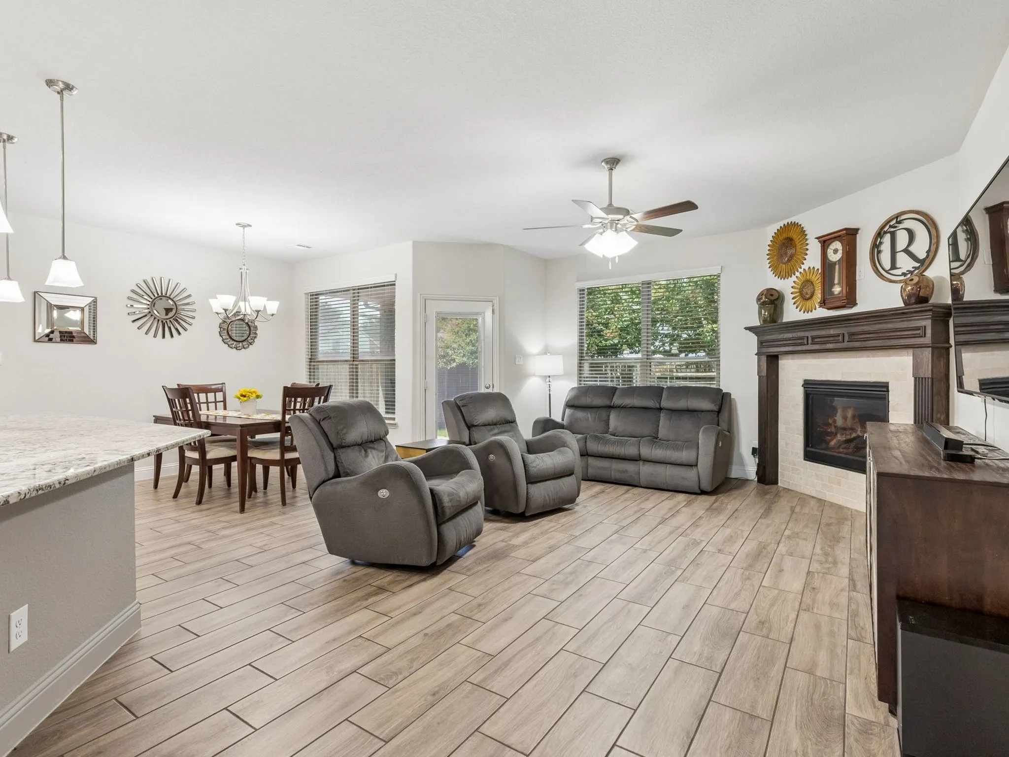 Wood-finish tile flooring throughout, a built-in fireplace with a stone surround and wood mantle, an overhead ceiling fan, and recessed lighting