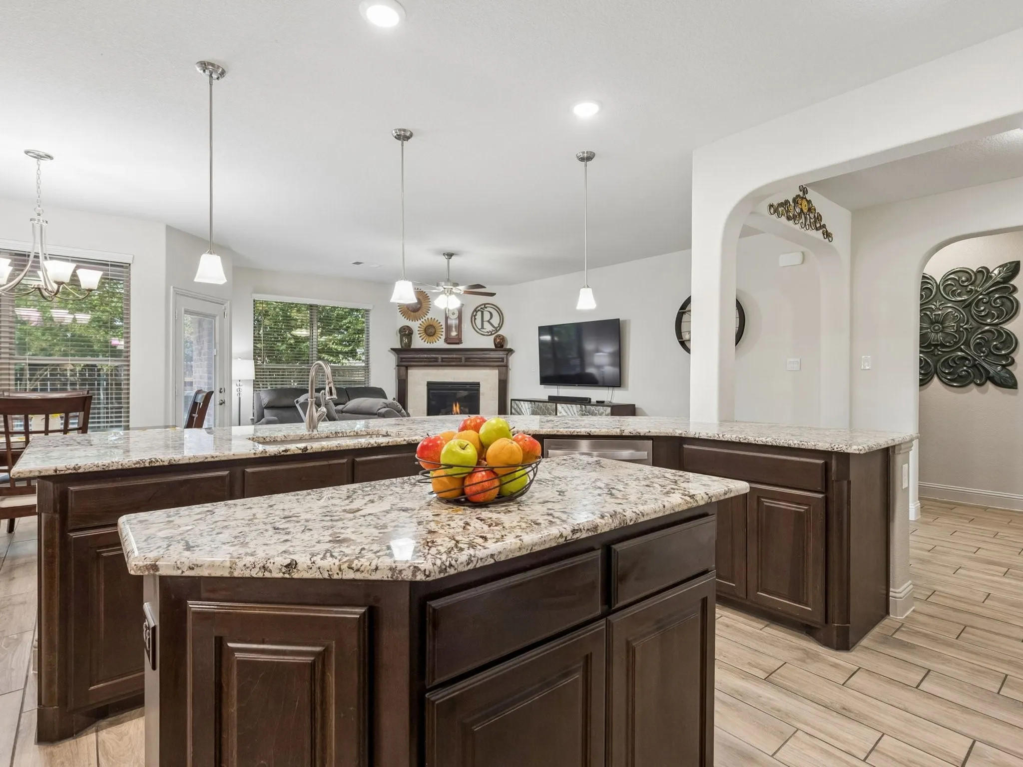 Kitchen island featuring granite countertops, dark wood cabinetry, pendant lighting, and wood-finish tile flooring