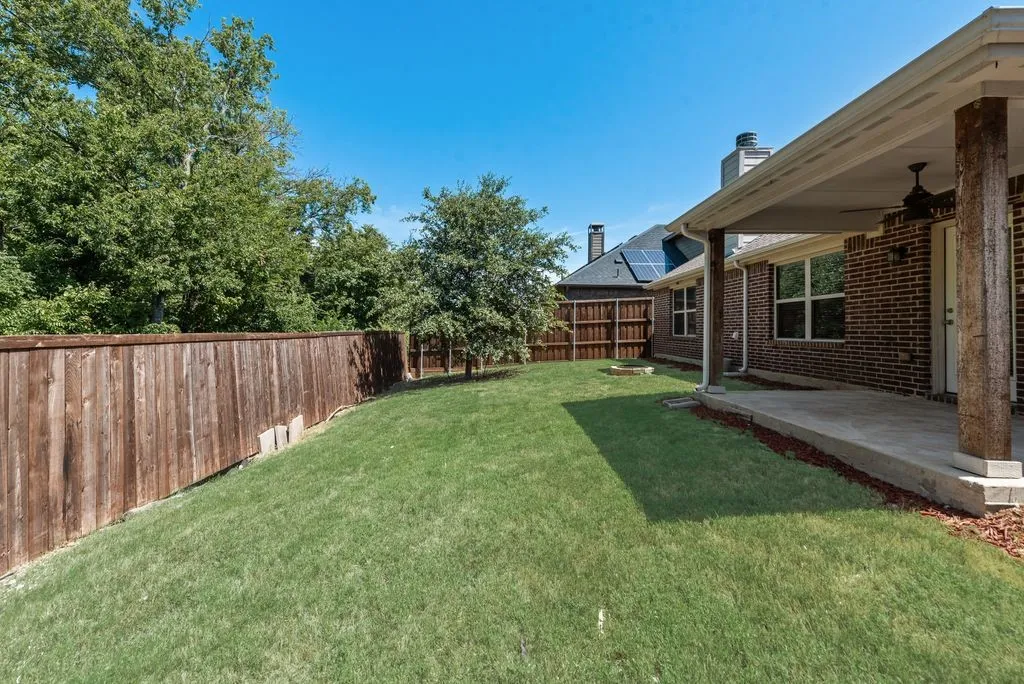 Spacious backyard featuring a covered patio, brick exterior, and a privacy fence