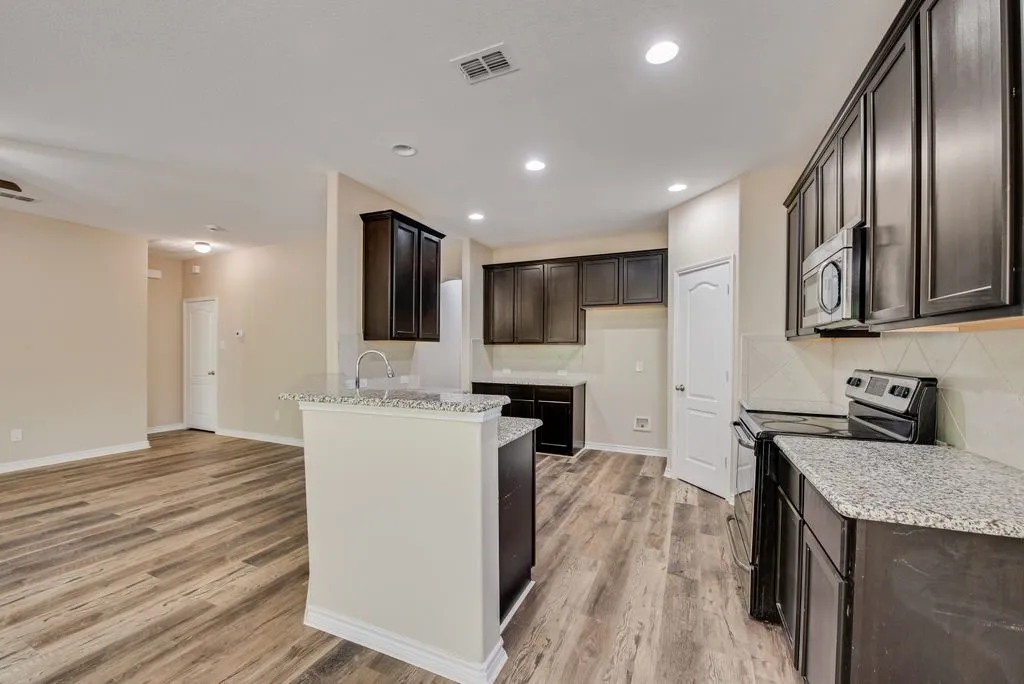 Open-concept kitchen featuring dark wood cabinetry, light-colored countertops, stainless steel appliances, and a central island with a sink